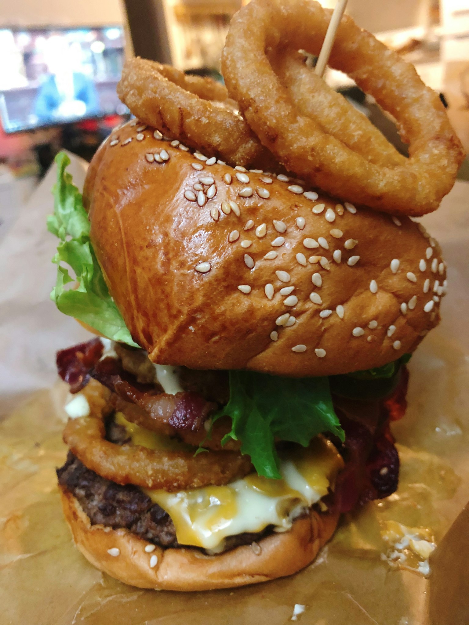 A towering hamburger topped with lettuce, cheese, bacon, and onion rings
