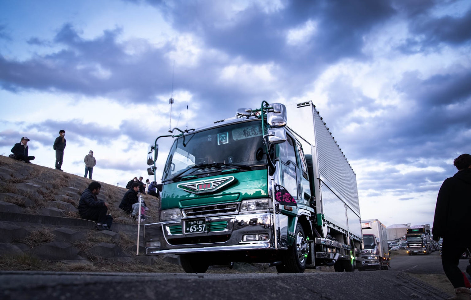 Truck driving under a blue sky with clouds and onlookers