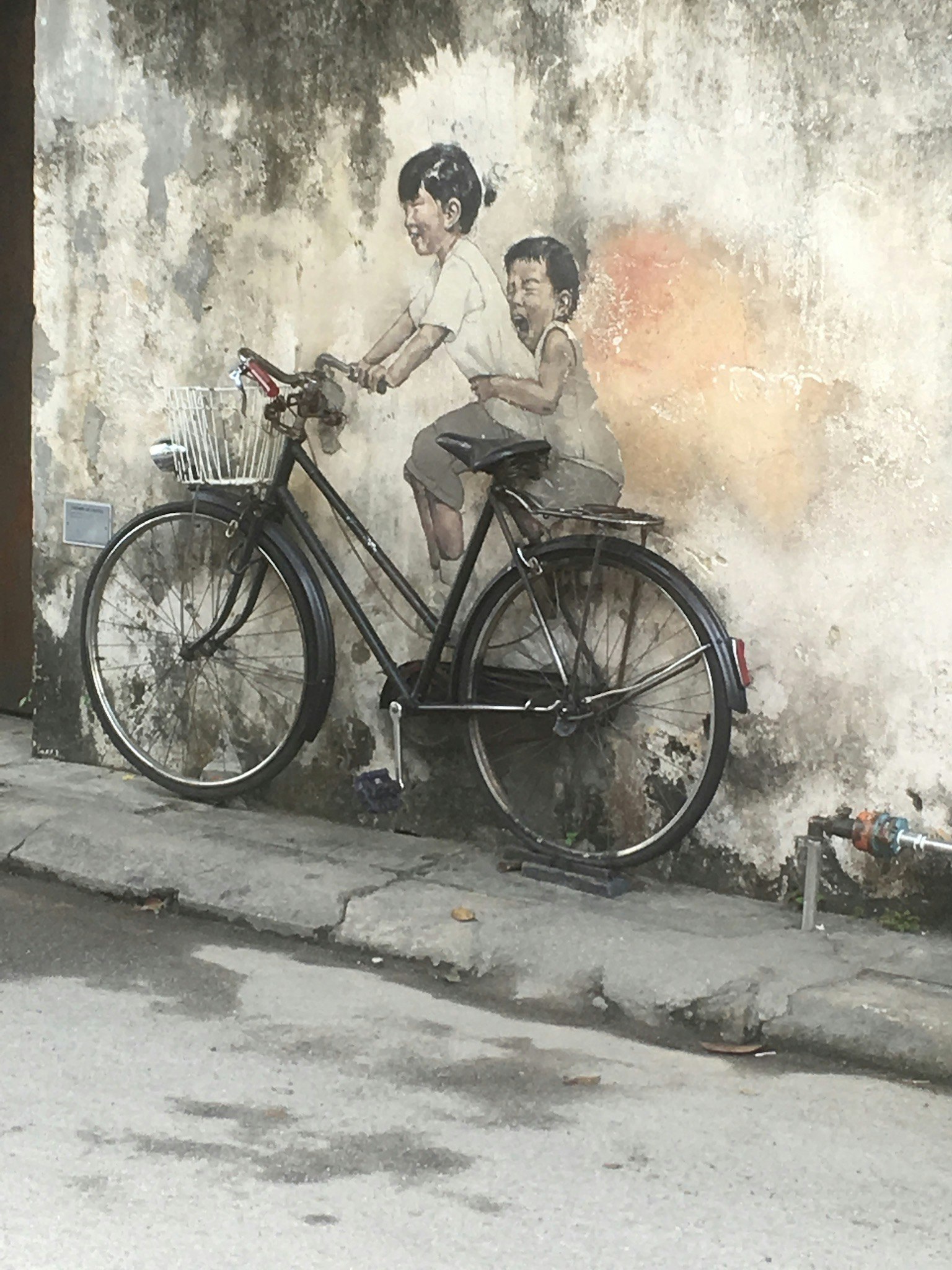Künstlerisches Wandbild mit Kindern auf einem Fahrrad vor einer verwitterten Wand