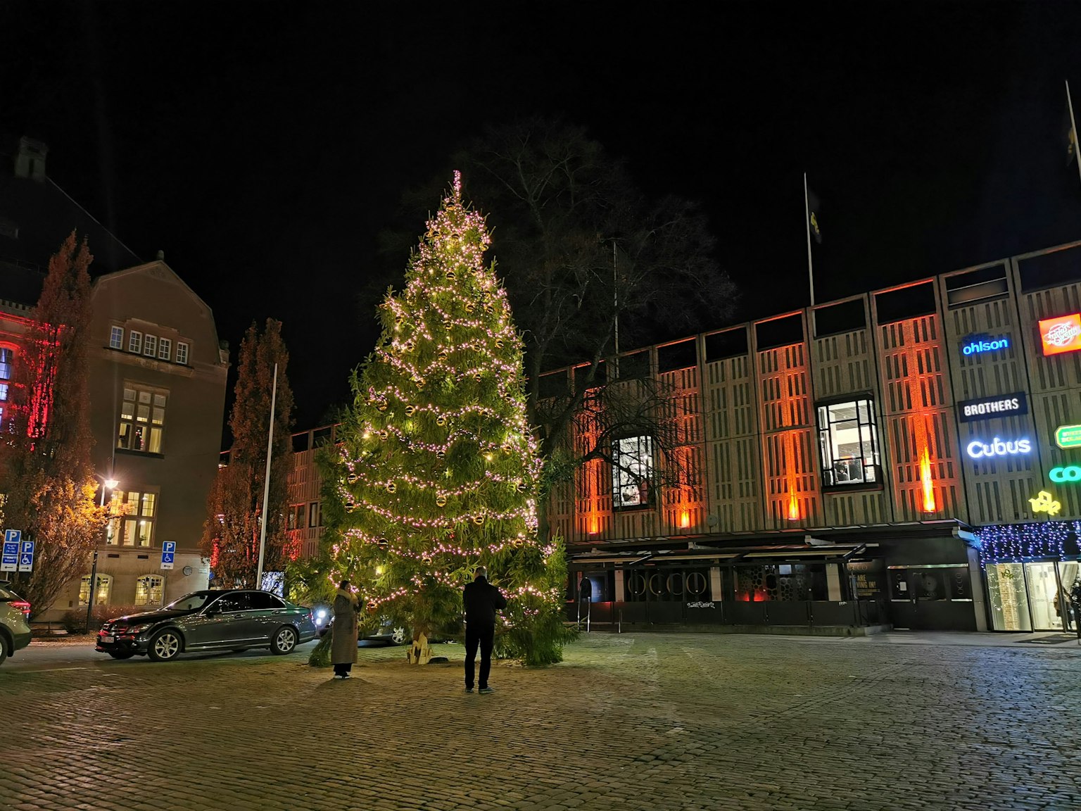 Grand arbre de Noël dans une place la nuit entouré de bâtiments éclairés