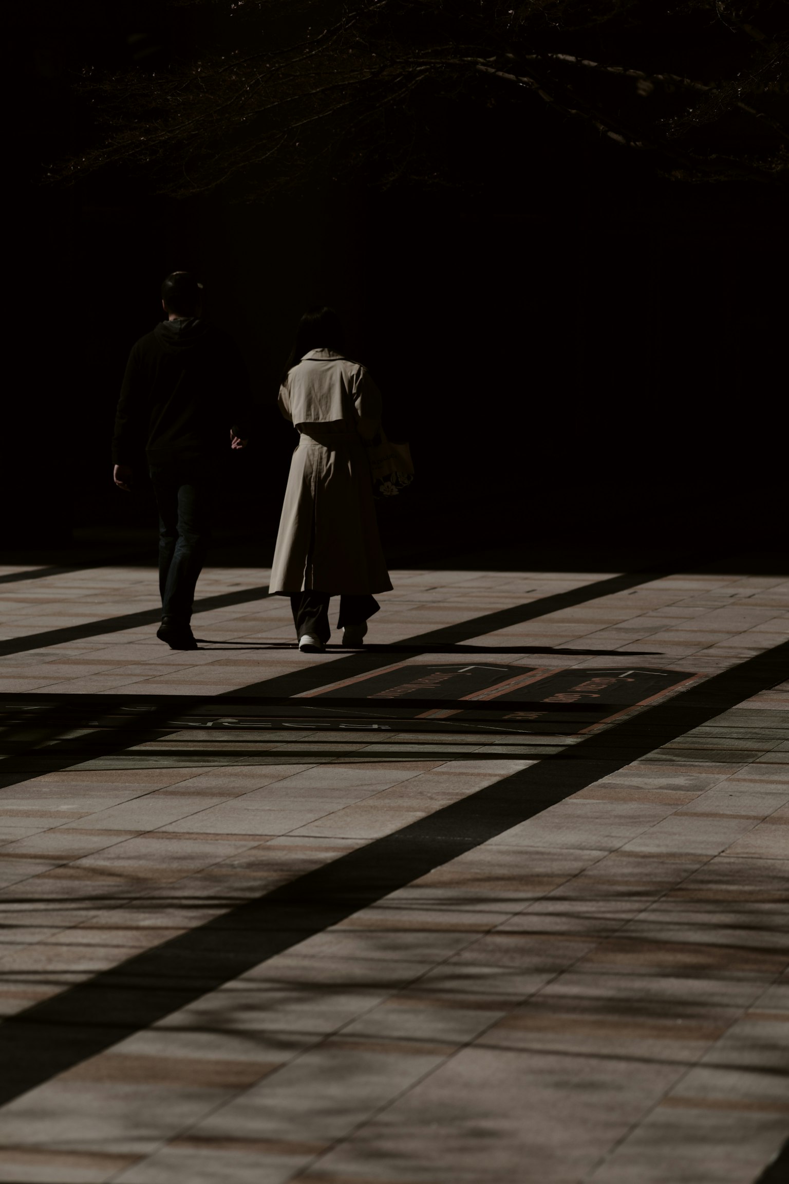 Silhouettes de deux personnes marchant dans l'ombre avec des motifs géométriques au sol