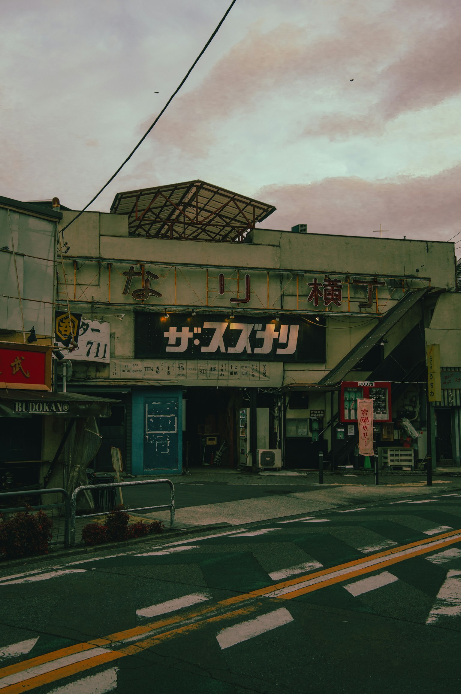 Exterior de un antiguo edificio comercial con letrero de estilo Showa y un cielo oscuro de fondo