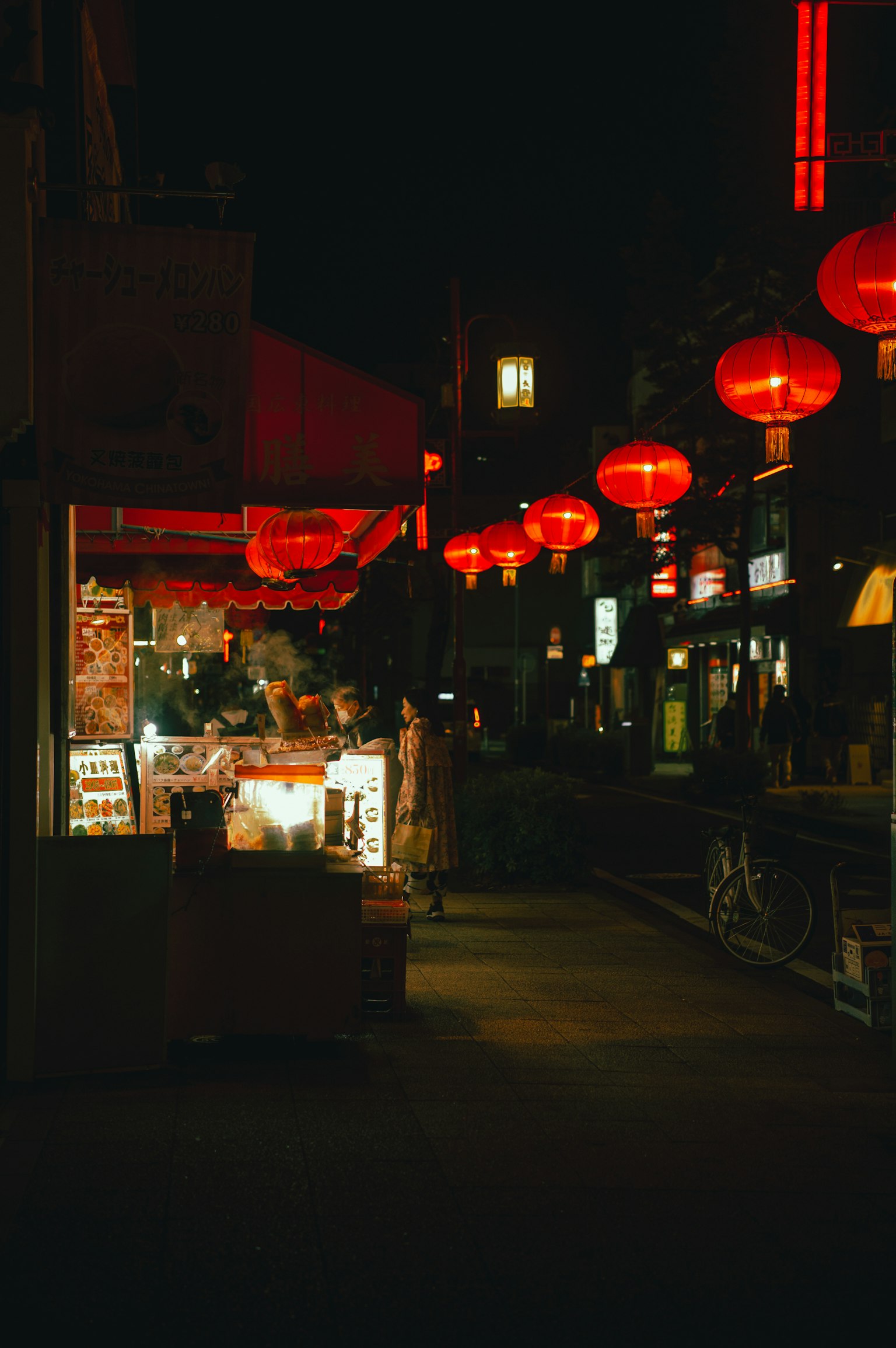 Une scène de rue la nuit avec des lanternes rouges illuminant une zone commerçante