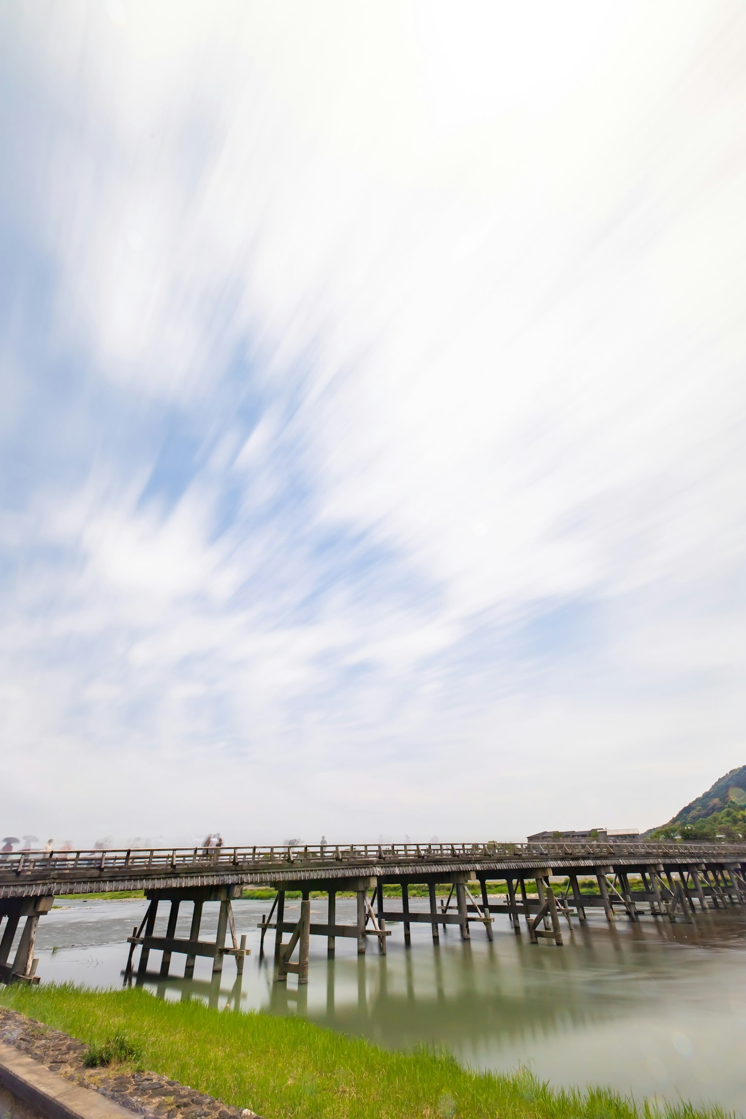 Holzbrücke über einen ruhigen Wasserlauf mit grünem Gras unter einem blauen Himmel