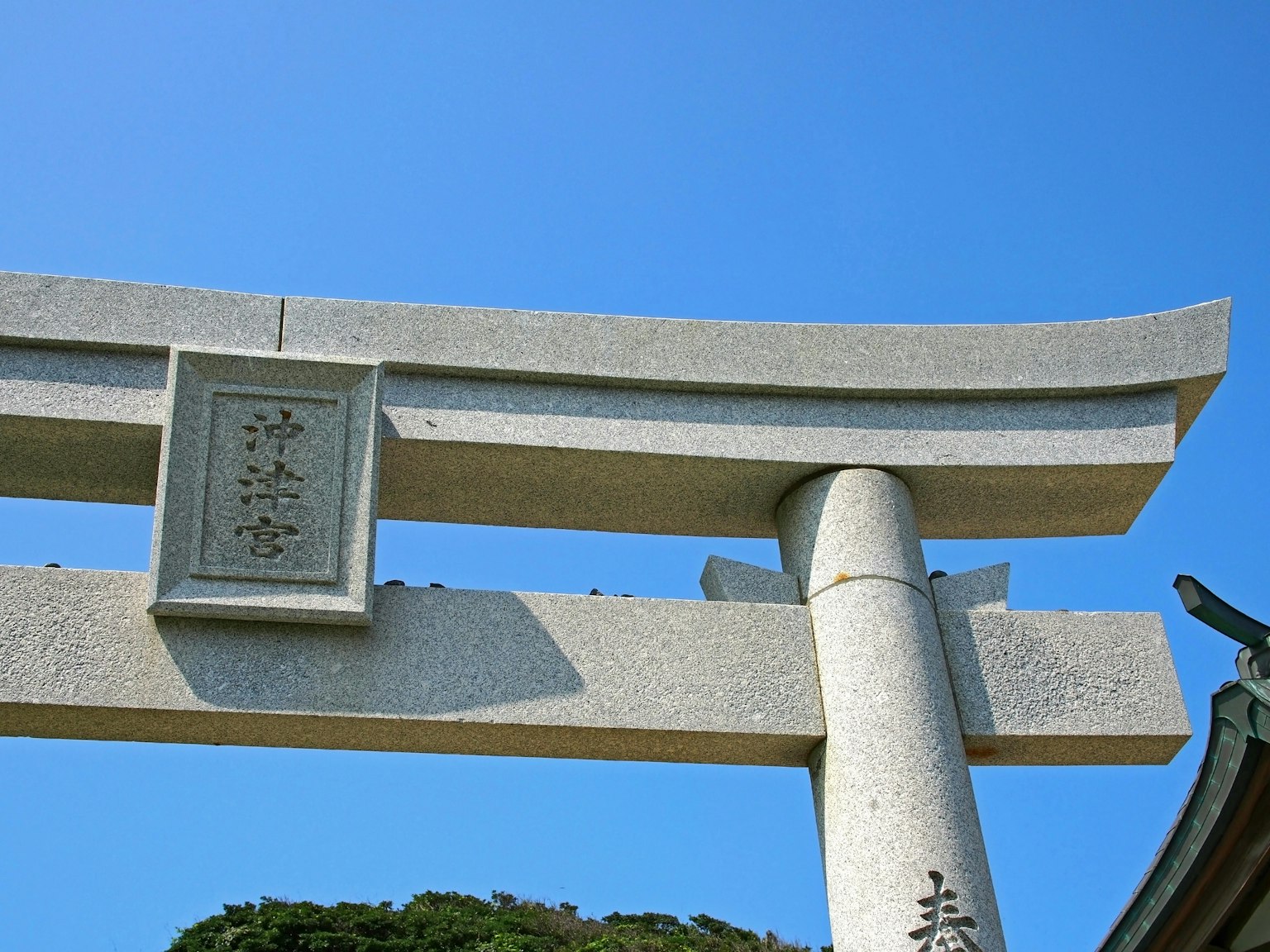 Puerta torii de piedra bajo un cielo azul con una placa de inscripción