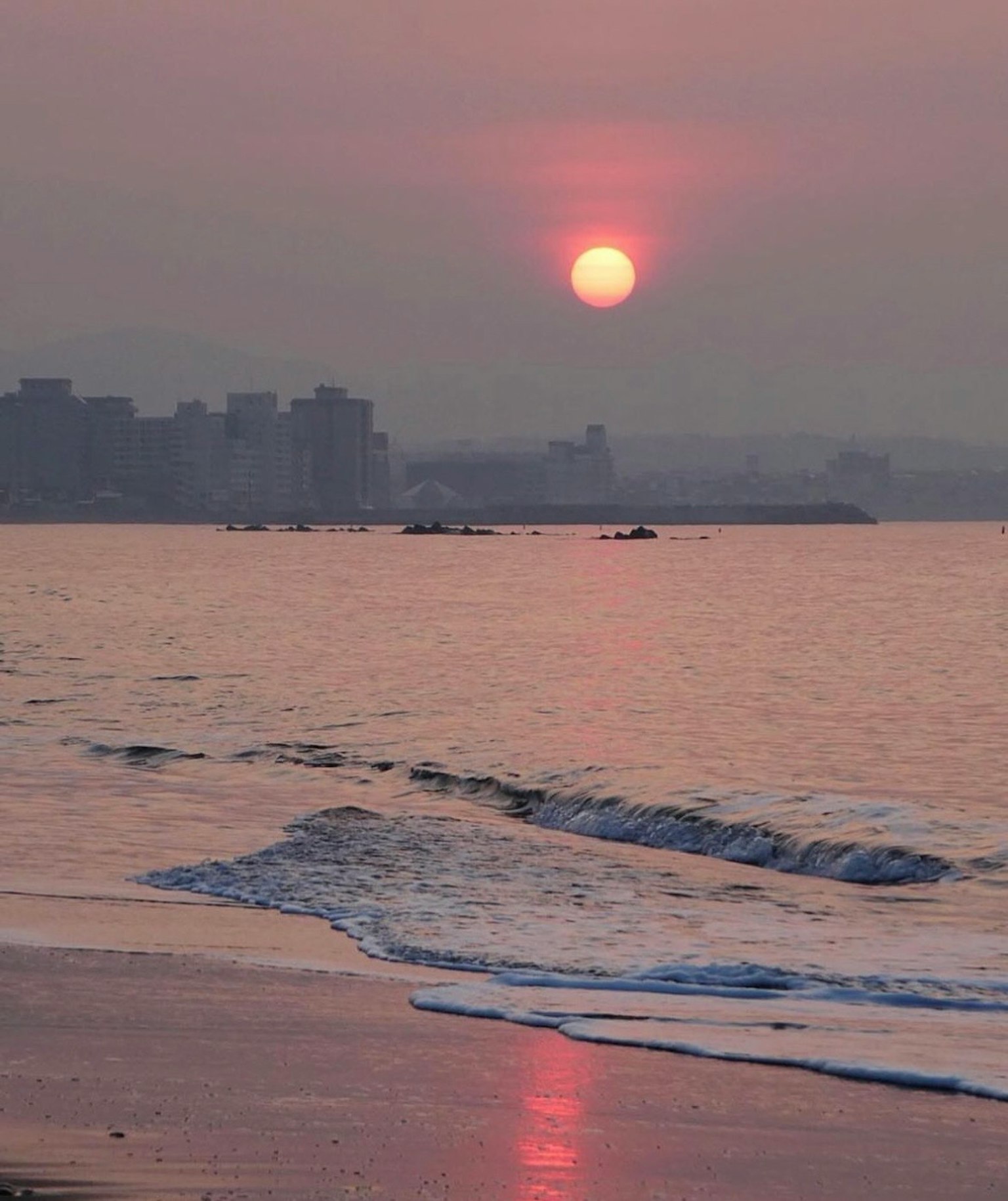 Tramonto sull'oceano con silhouette di città e riflessi delle onde