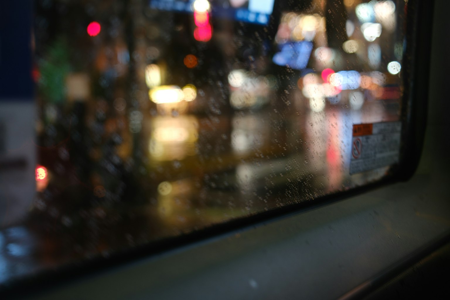 雨に濡れた窓越しの夜の都市景観とぼやけた光