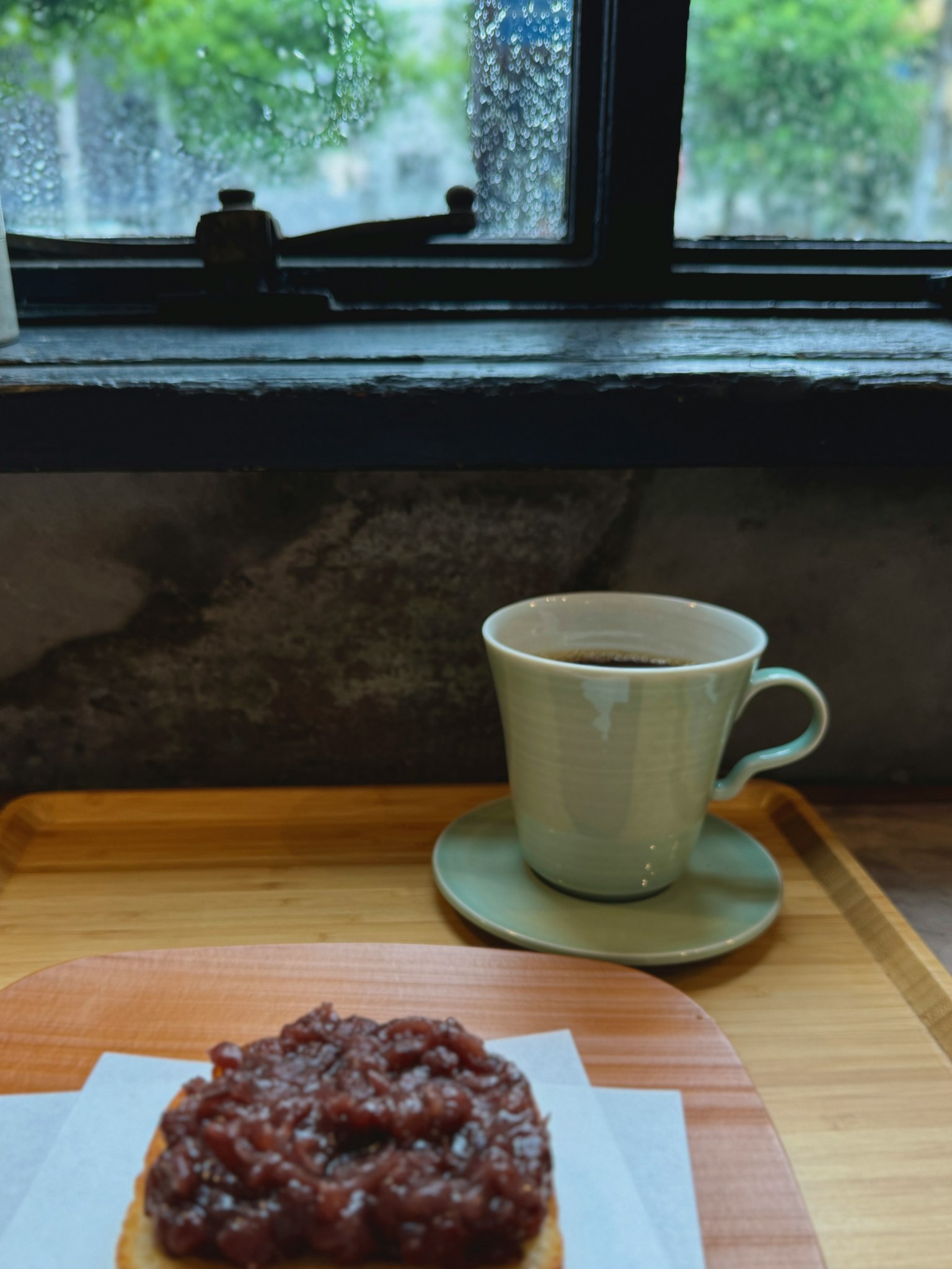 Ein Cafétisch mit einer Tasse Kaffee und einem Toast mit roter Bohnenpaste bei Regen, der durch das Fenster sichtbar ist