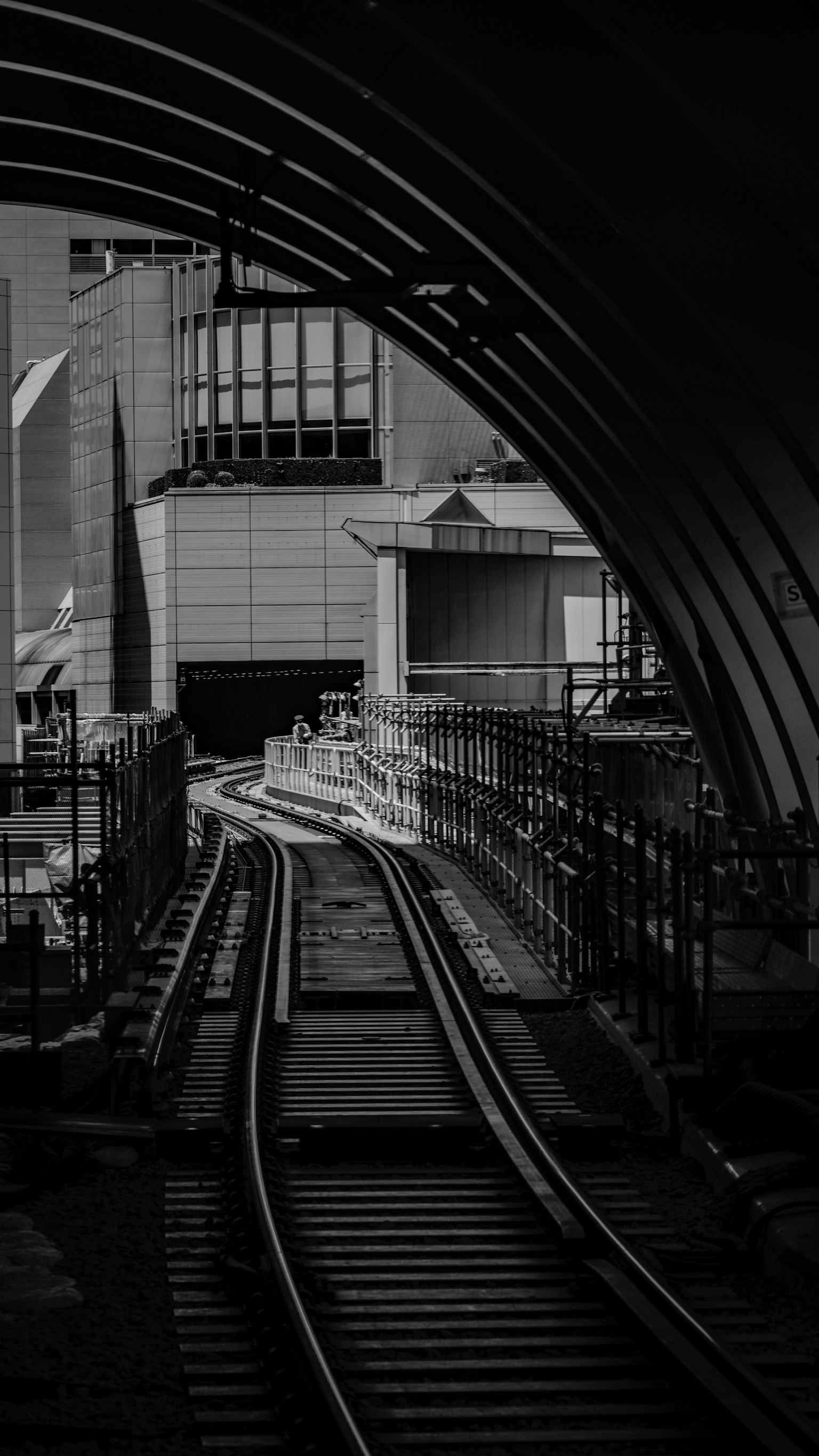 Photo en noir et blanc de voies ferrées à l'intérieur d'un tunnel avec des structures de bâtiment visibles