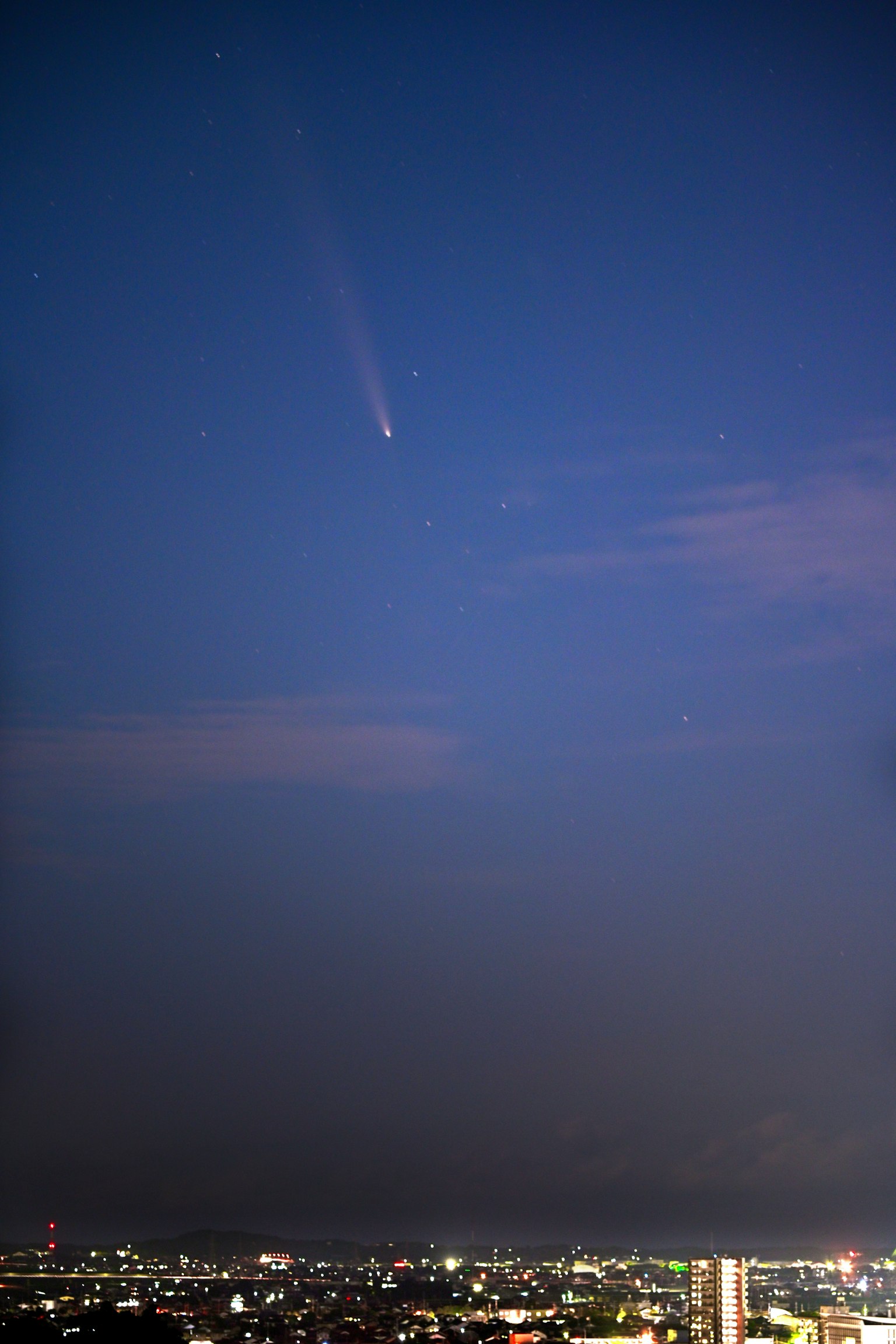 Cola de cometa apareciendo en el cielo nocturno con las luces de la ciudad abajo