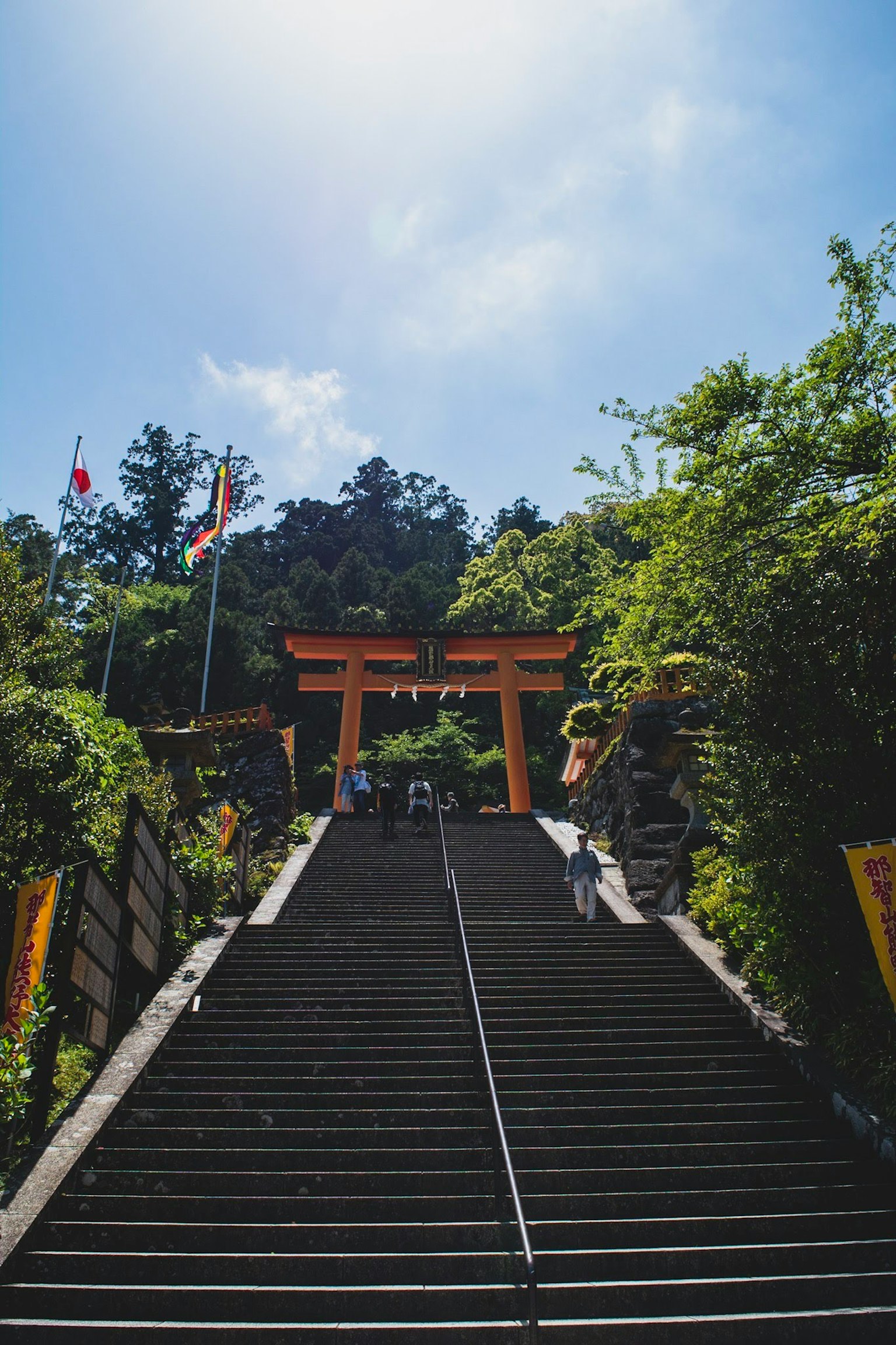 Staircase leading to a torii gate surrounded by greenery and blue sky