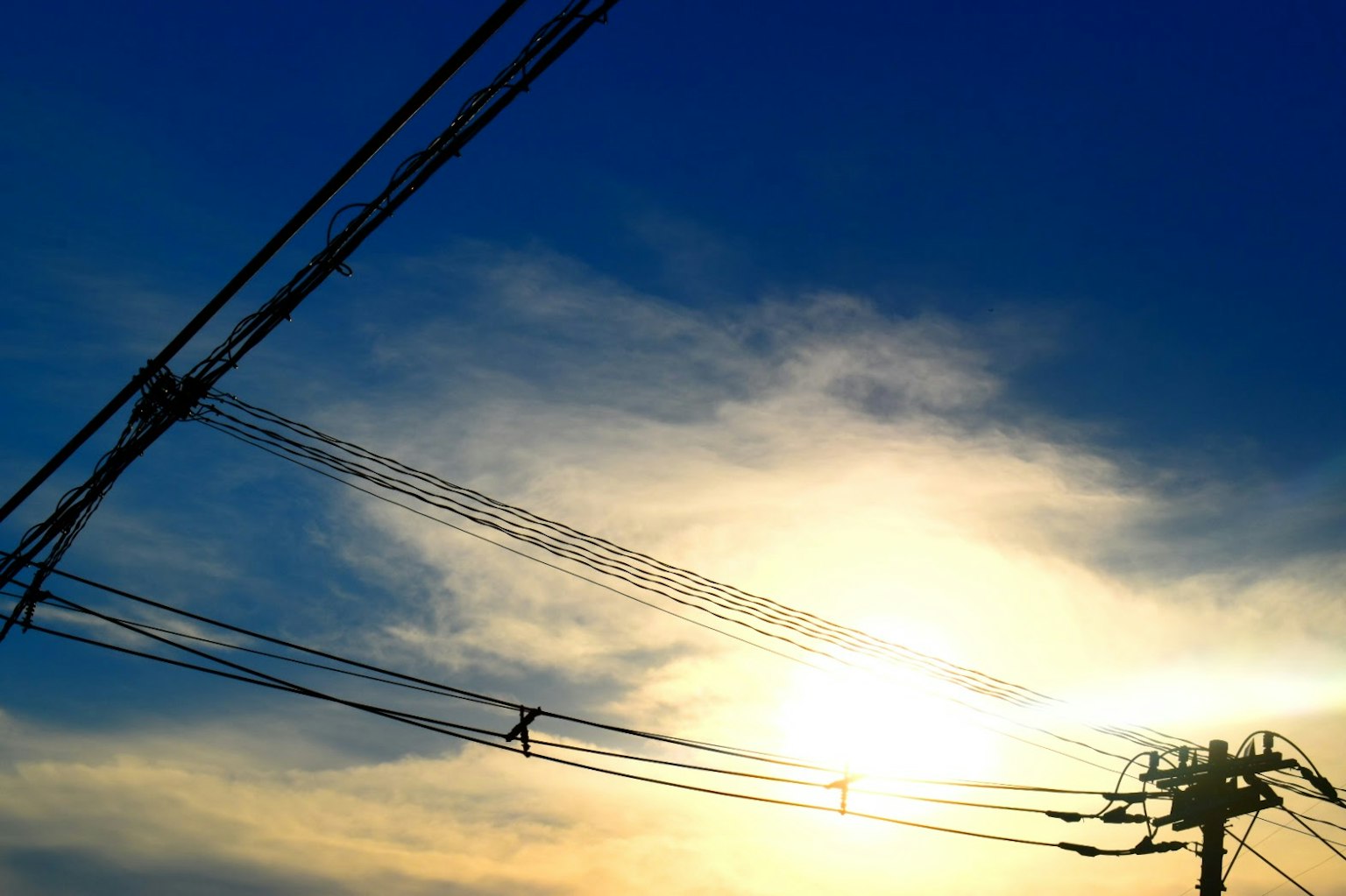 Siluet kabel listrik di latar belakang langit biru dengan awan dan sinar matahari