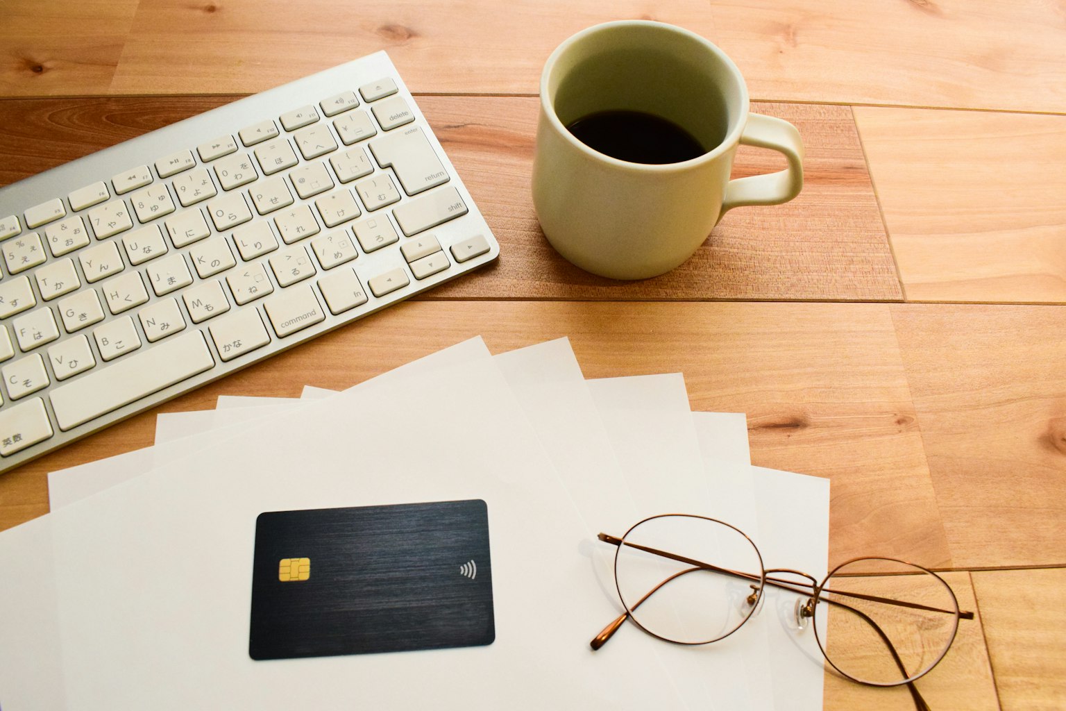 Une scène de bureau avec des papiers blancs une carte de crédit noire des lunettes une tasse verte et un clavier