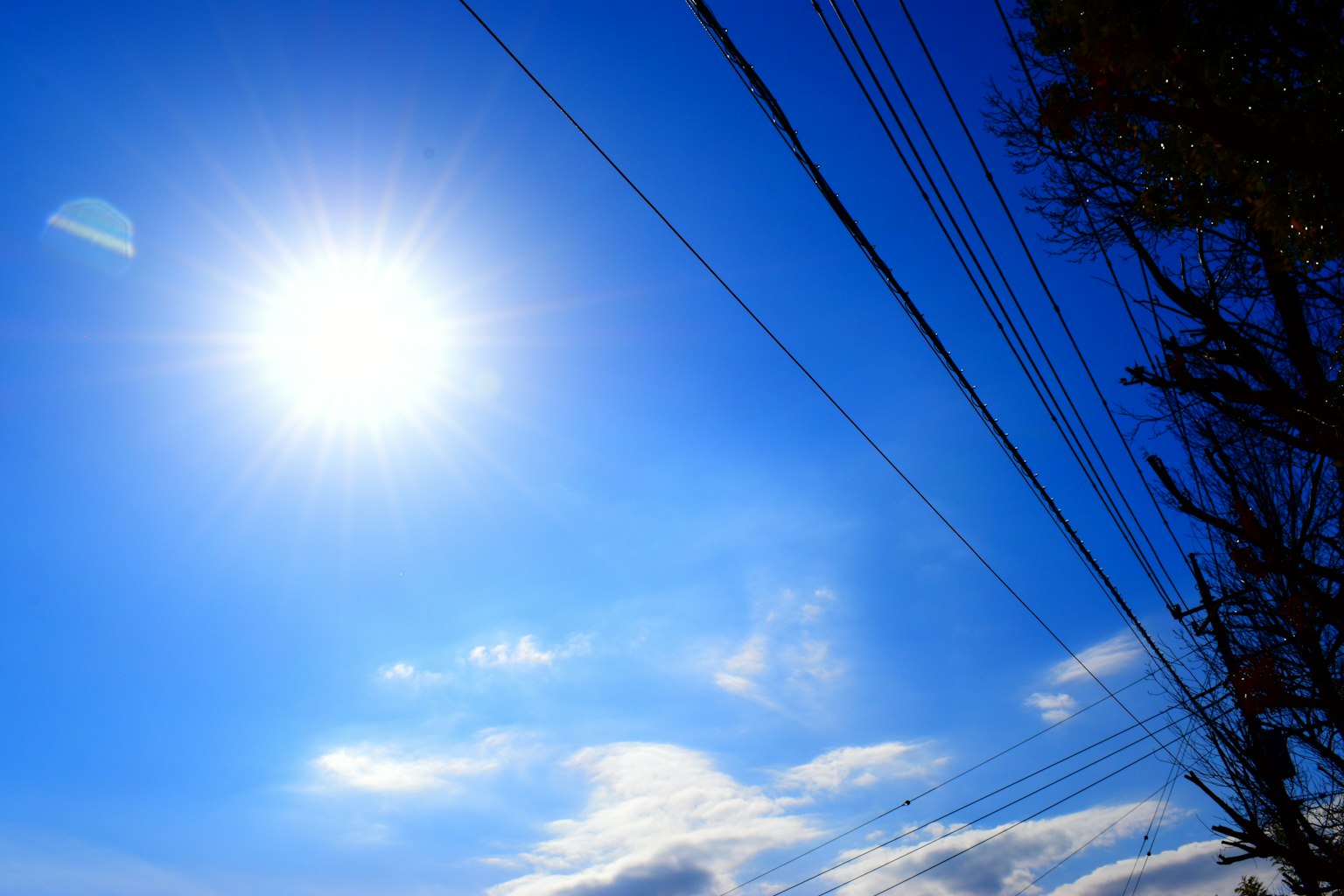 Sole luminoso in un cielo azzurro con nuvole e linee elettriche a destra