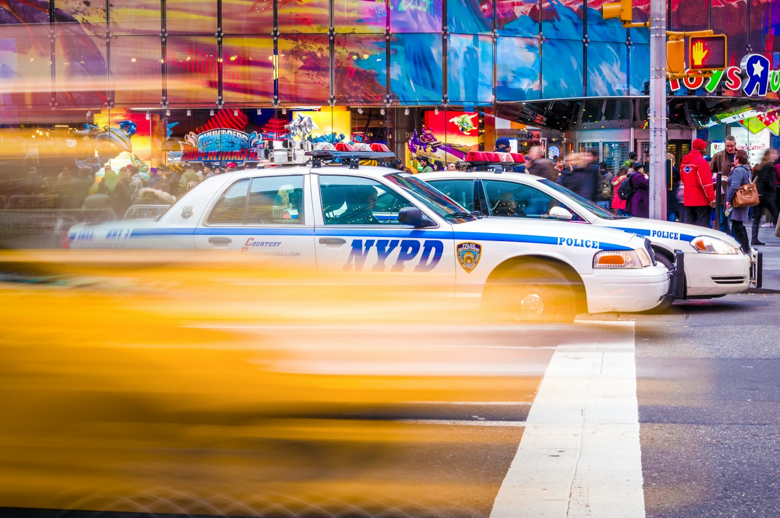 Escena de un taxi amarillo pasando junto a coches de policía NYPD en una intersección concurrida