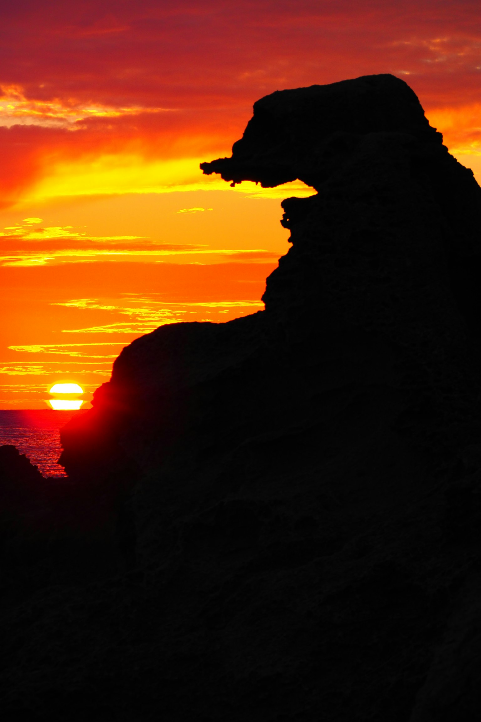 Silhouette of a rock formation against a vibrant sunset