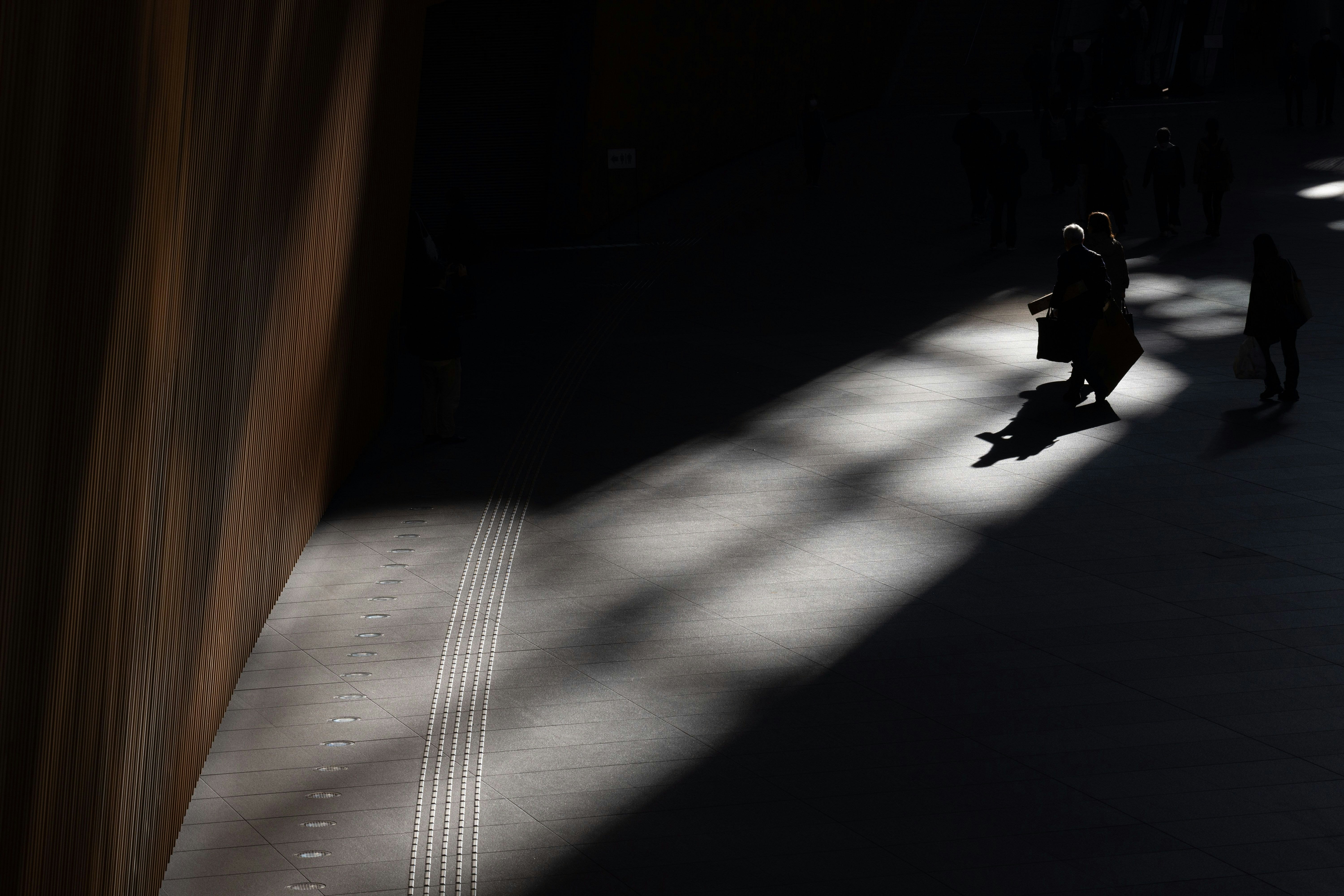 Schatten von Menschen, die entlang einer dunklen Gassenwand mit Lichtstrahlen gehen