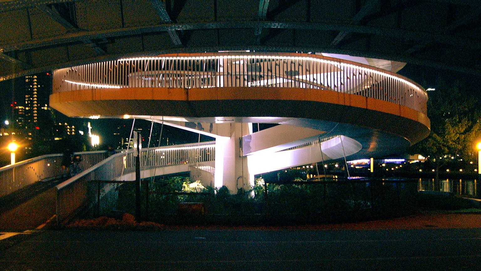 Puente peatonal en espiral iluminado por la noche en un entorno urbano