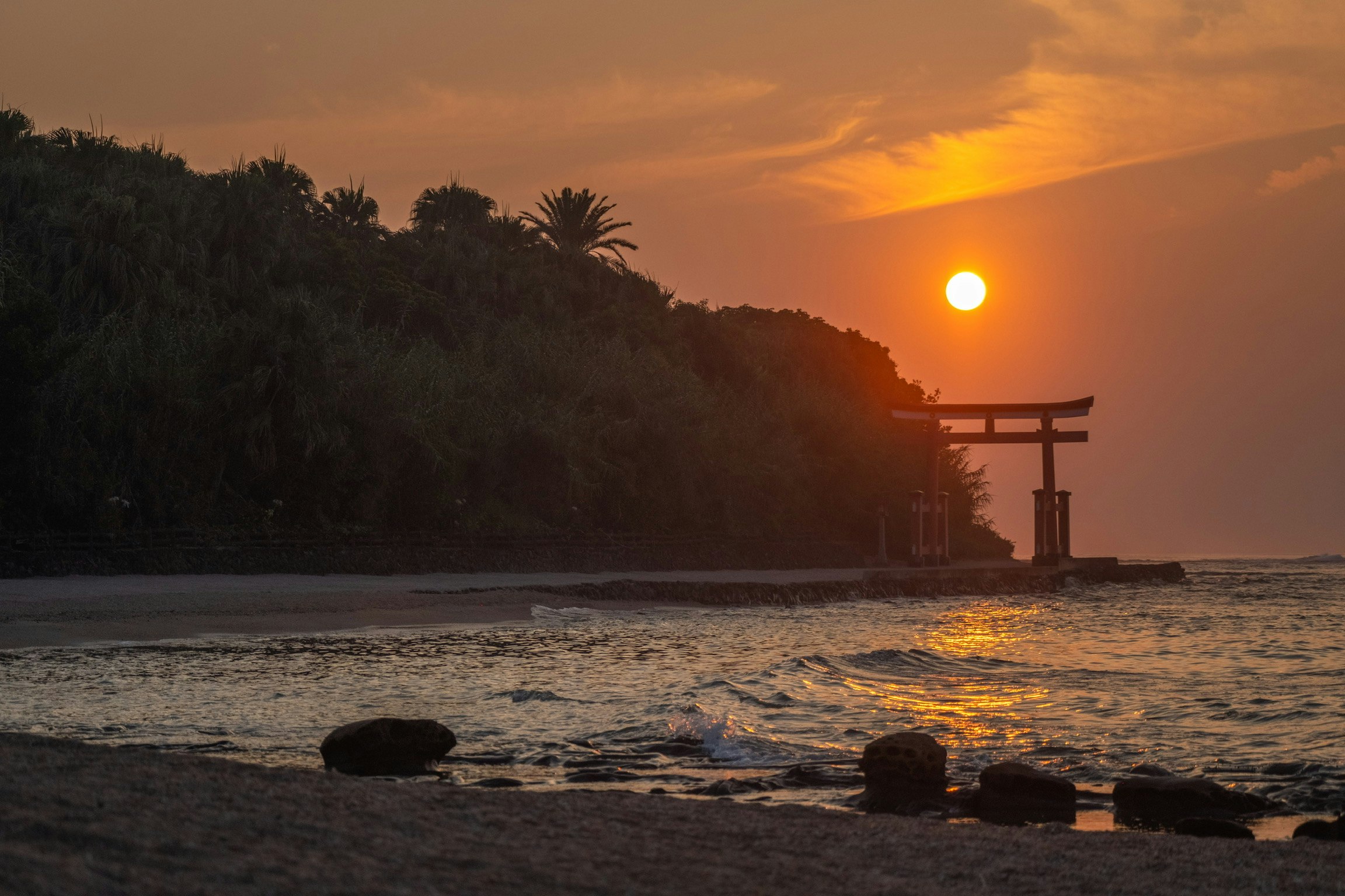 夕日と鳥居が立つ海辺の砂浜の風景