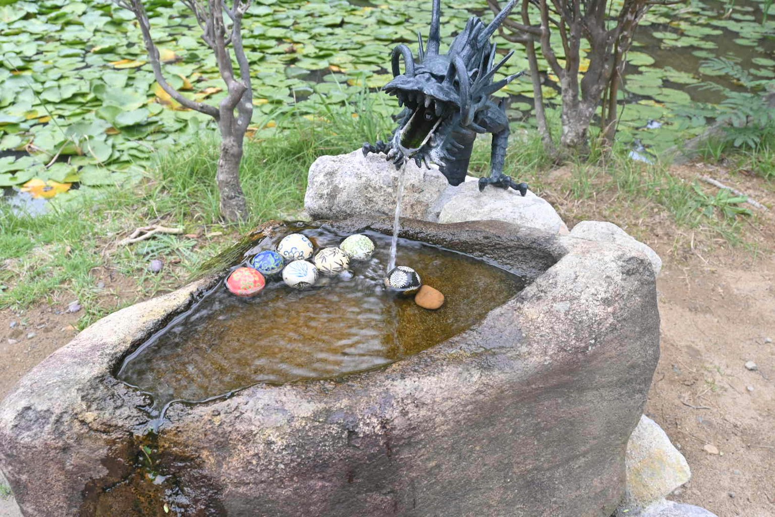 龍雕塑從石頭噴泉噴出水，周圍有五彩石頭