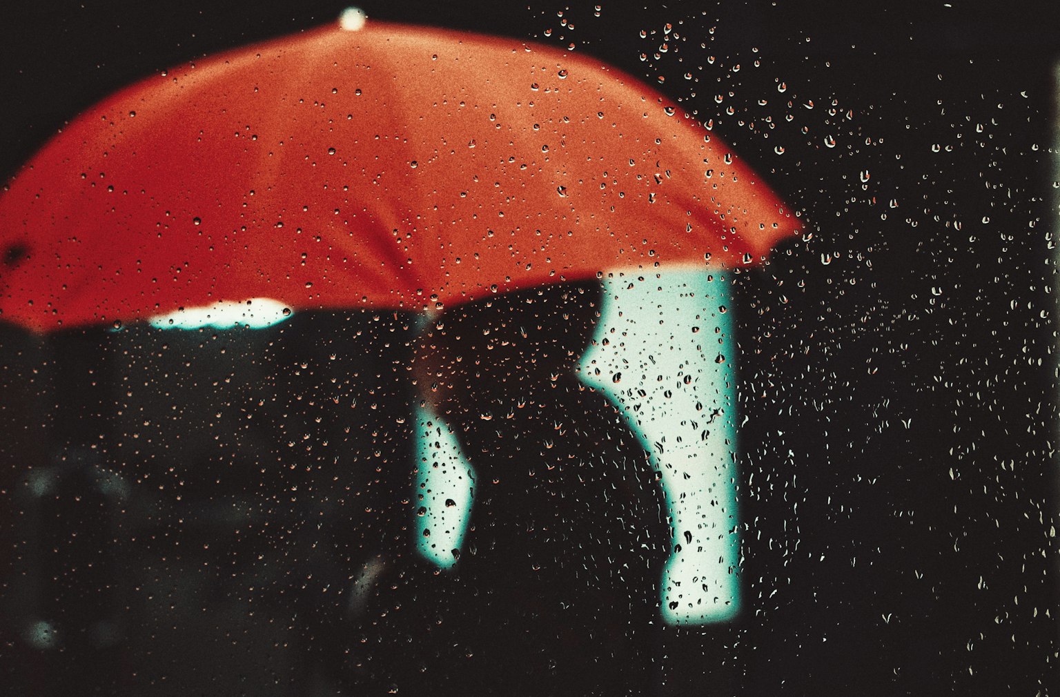 เงาร่างใต้ร่มแดงพร้อมกับหยดน้ำฝนที่โฟกัส