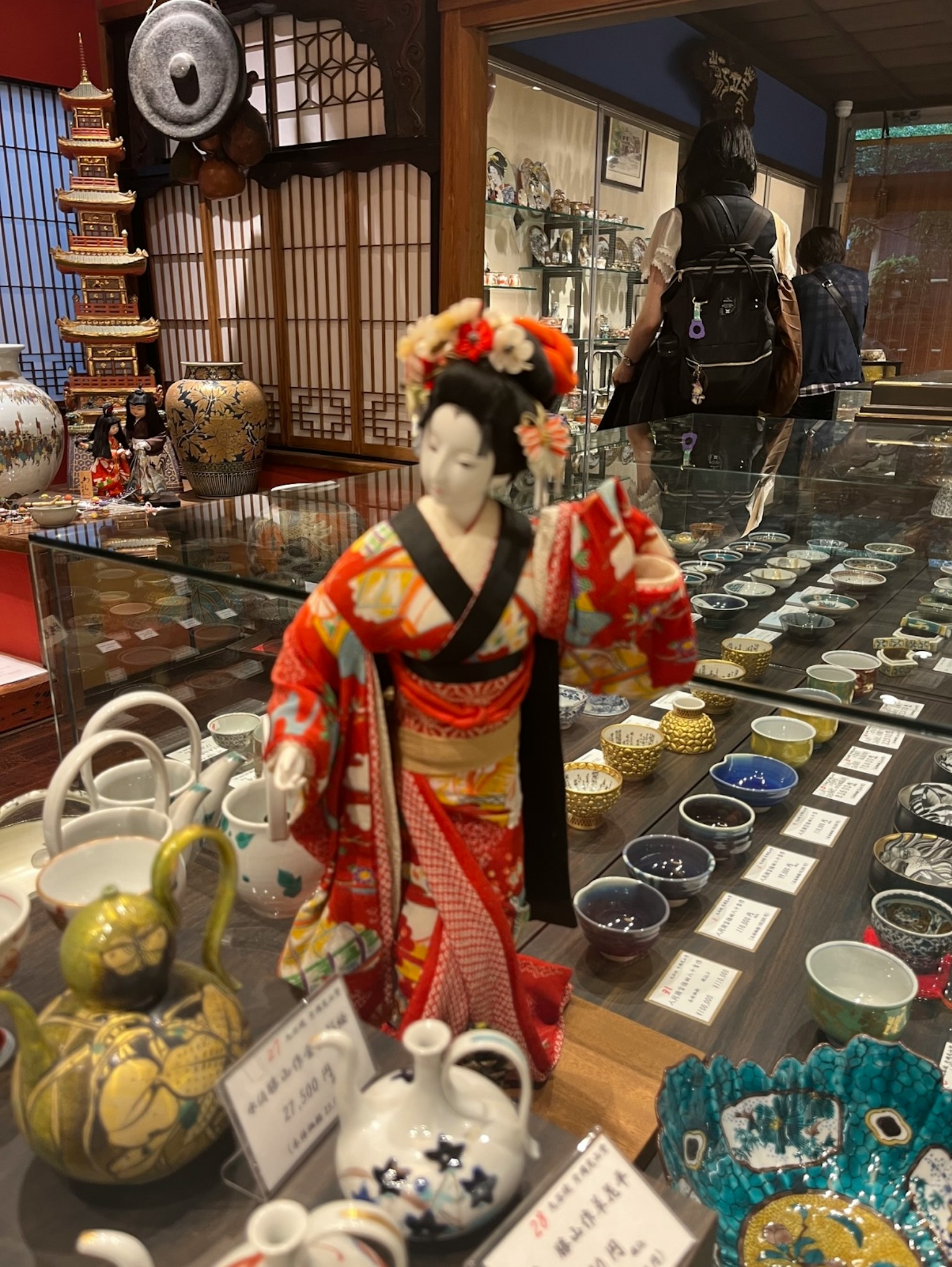 Boneka Jepang dalam kimono merah dipajang di toko yang dipenuhi keramik