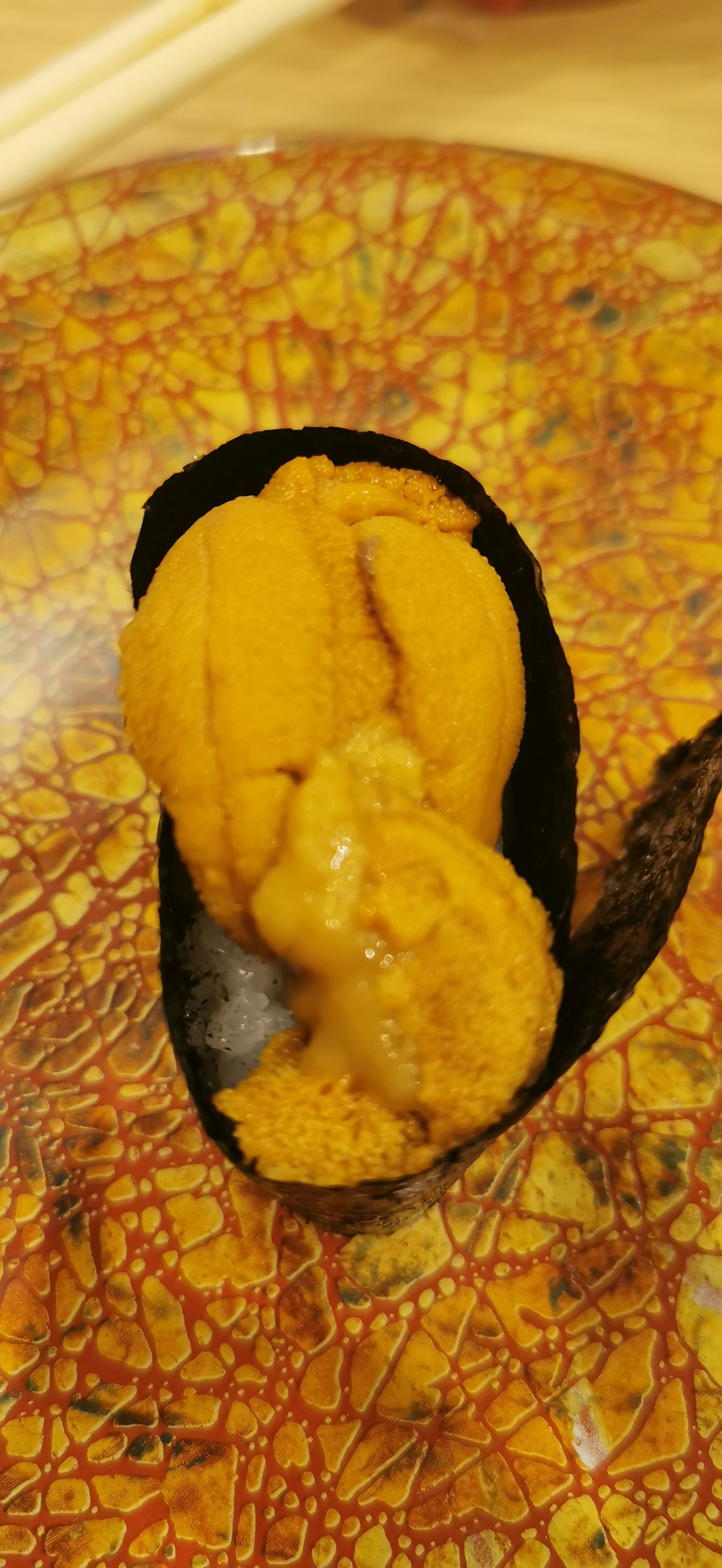 Un morceau de sushi avec un oursin orange vif servi sur une assiette japonaise décorative