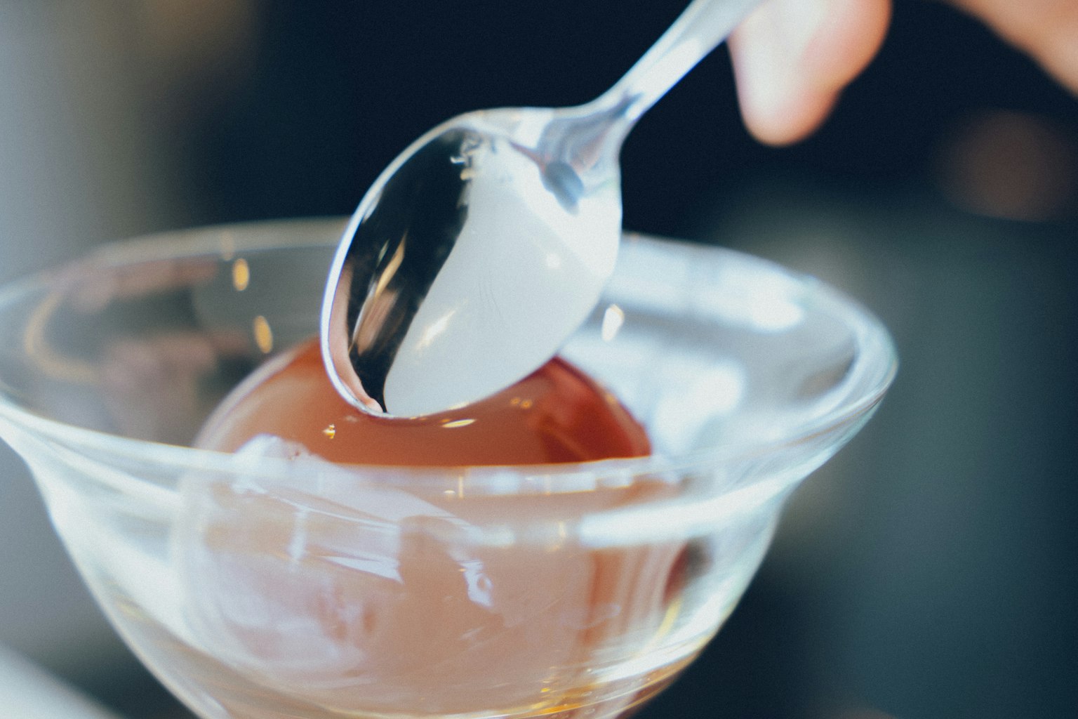 A hand holding a spoon scooping a red dessert from a clear bowl