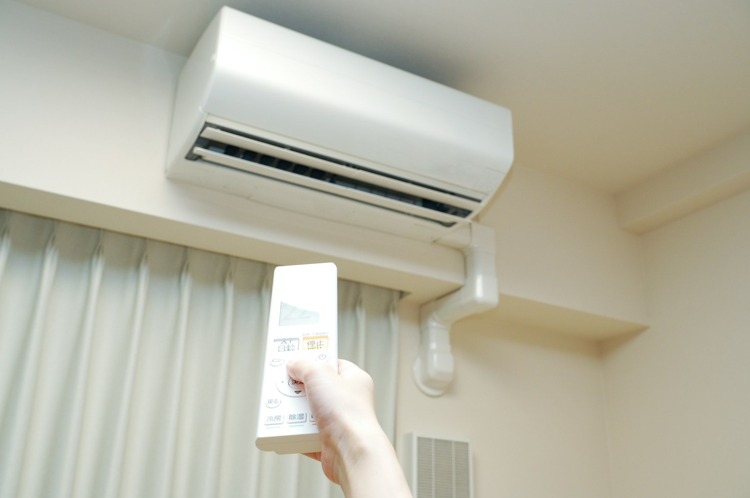 Main tenant une télécommande de climatiseur avec un climatiseur mural