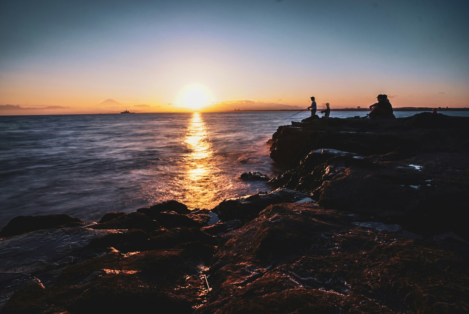 silhouetted fishermen on rocky shoreline at sunset