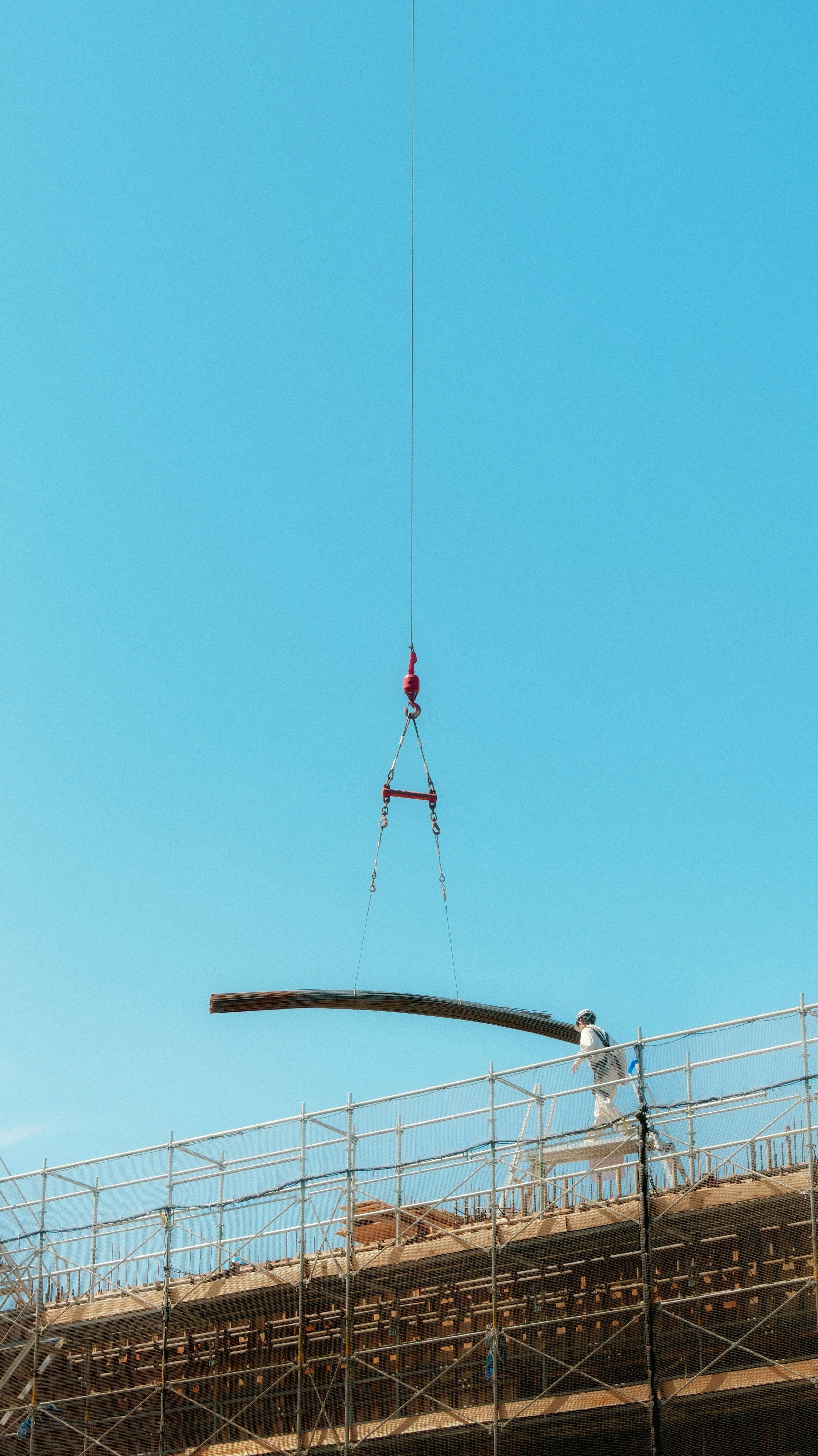 青空の下でクレーン作業をする作業員のいる建設現場