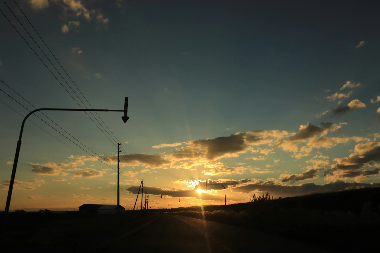 Tramonto su una strada con linee elettriche e nuvole