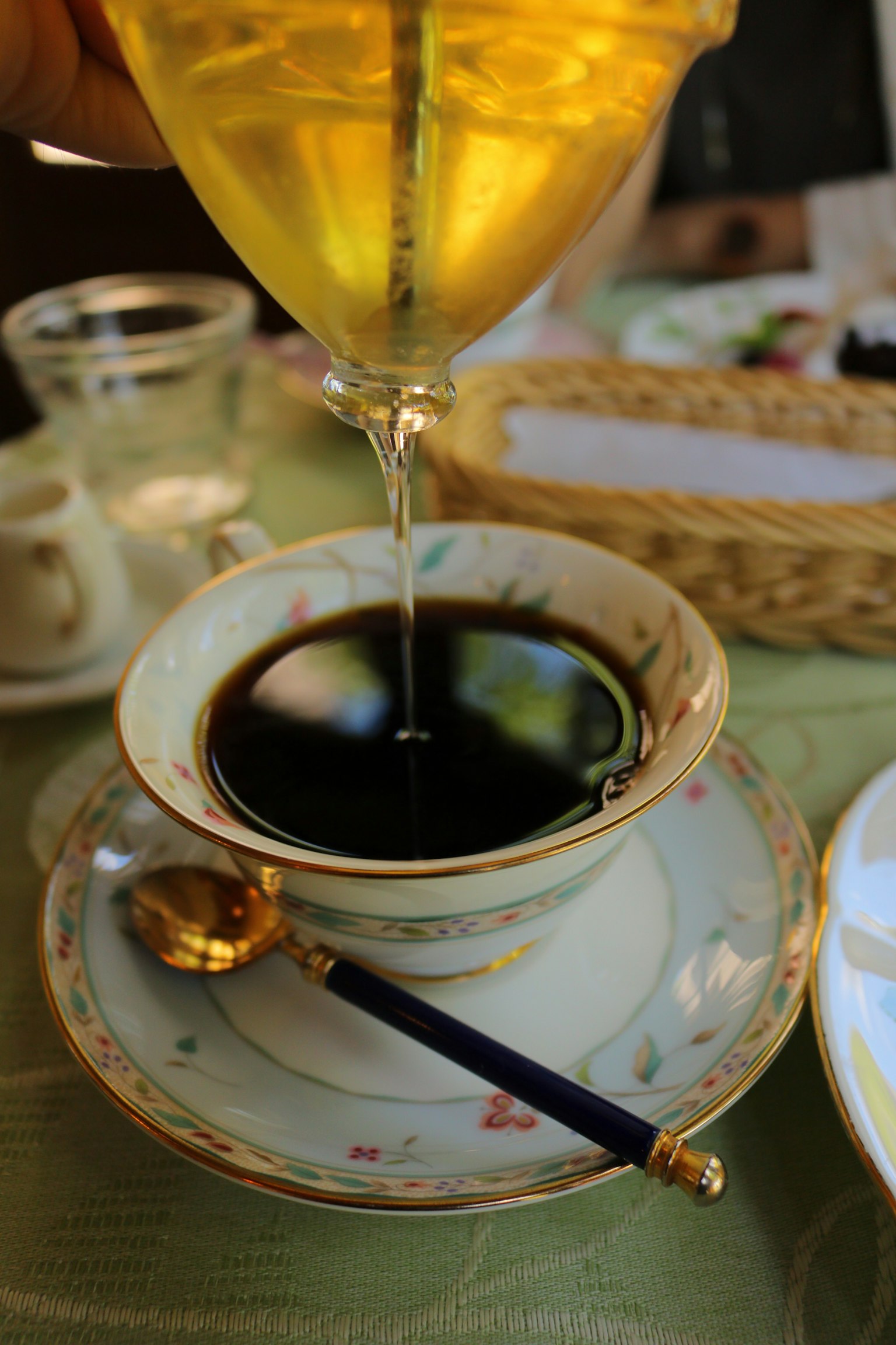 กาแฟเข้มถูกเทลงในถ้วยสีครีมที่ละเอียดอ่อนพร้อมช้อนทอง