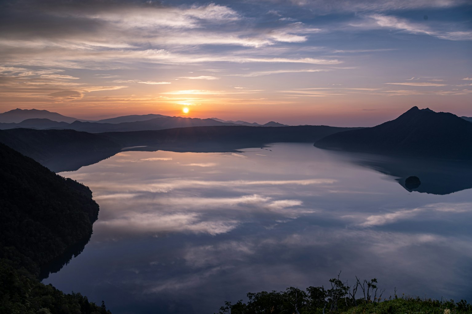 Malersicher Blick auf einen Sonnenuntergang, der sich auf einem See spiegelt, umgeben von Bergen