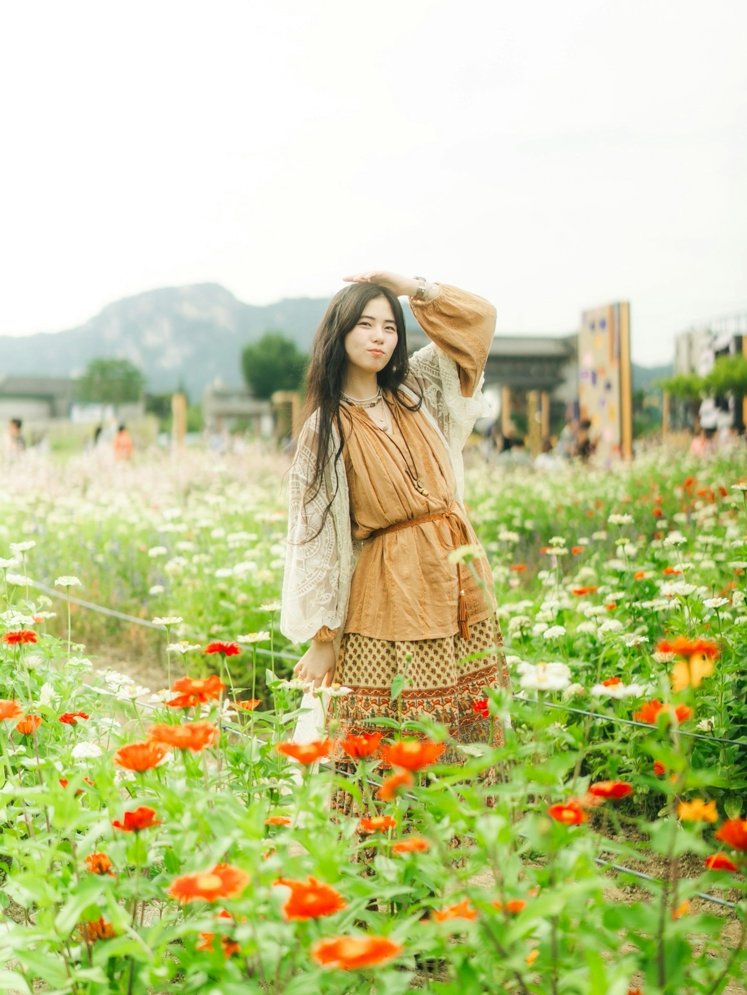 花畑でポーズをとる女性の写真 緑と色とりどりの花々が広がる風景