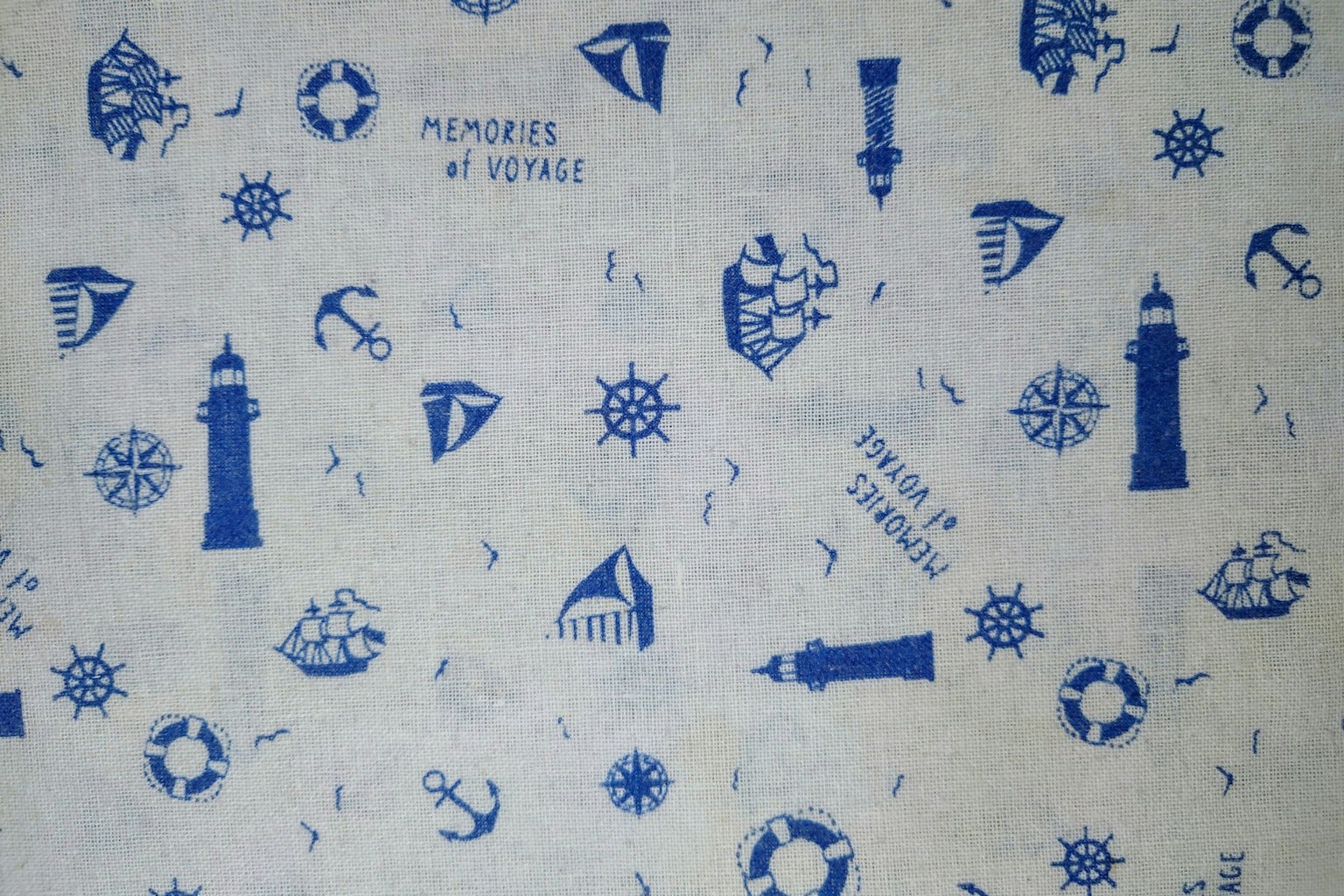 Fabric with a nautical theme featuring blue illustrations of lighthouses, ships, anchors, stars, and marine icons