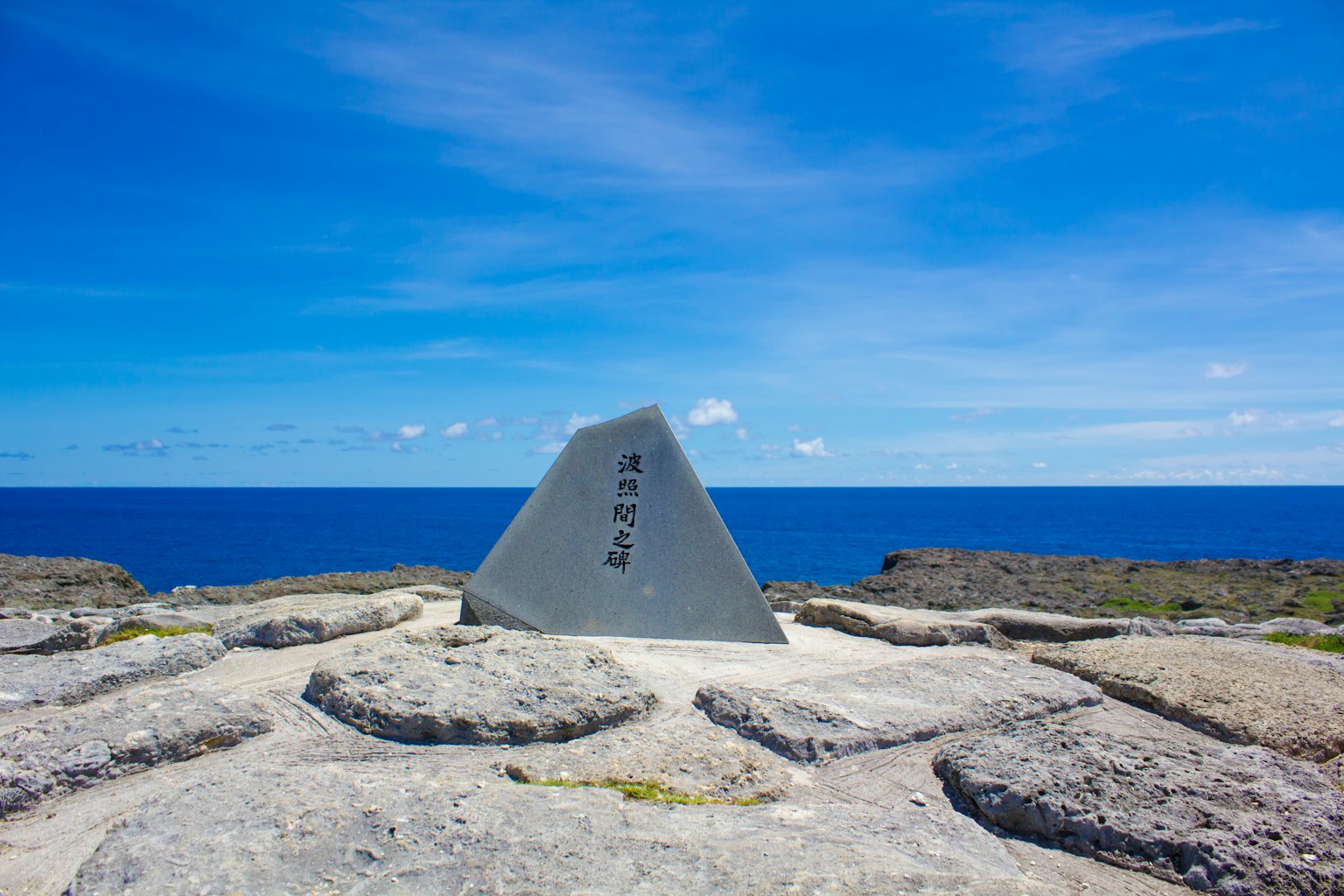 Monumento triangolare con iscrizioni contro un cielo blu e oceano