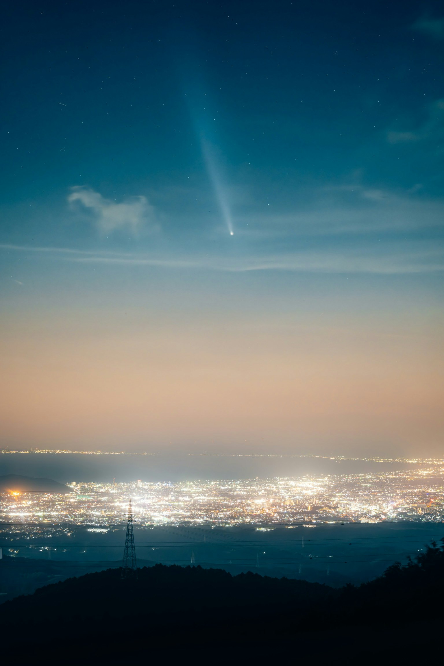 夜空に輝く彗星と都市の明かりが広がる風景