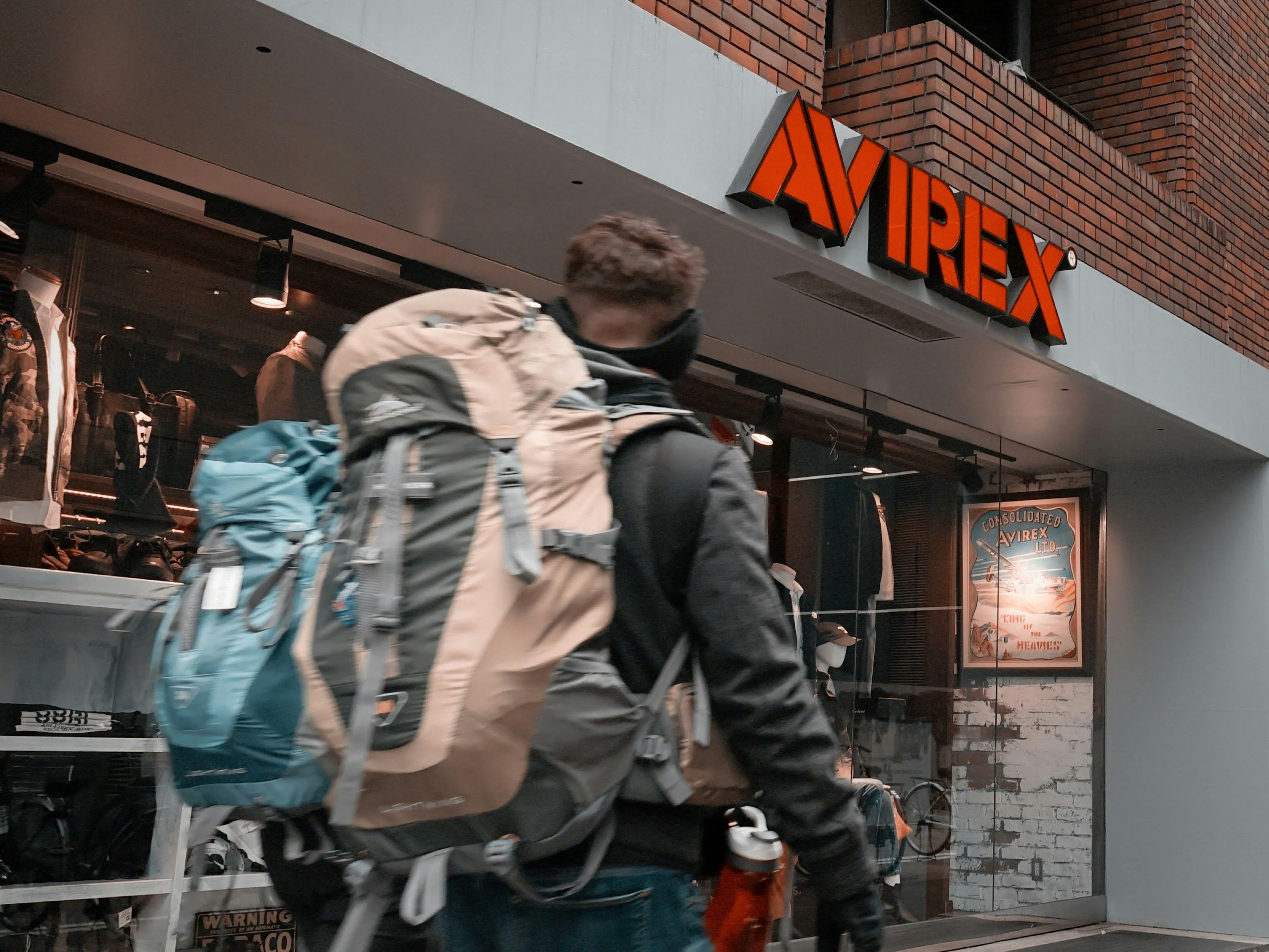 レンガ壁の店舗前で大きなリュックを背負う外国人男性のスナップ