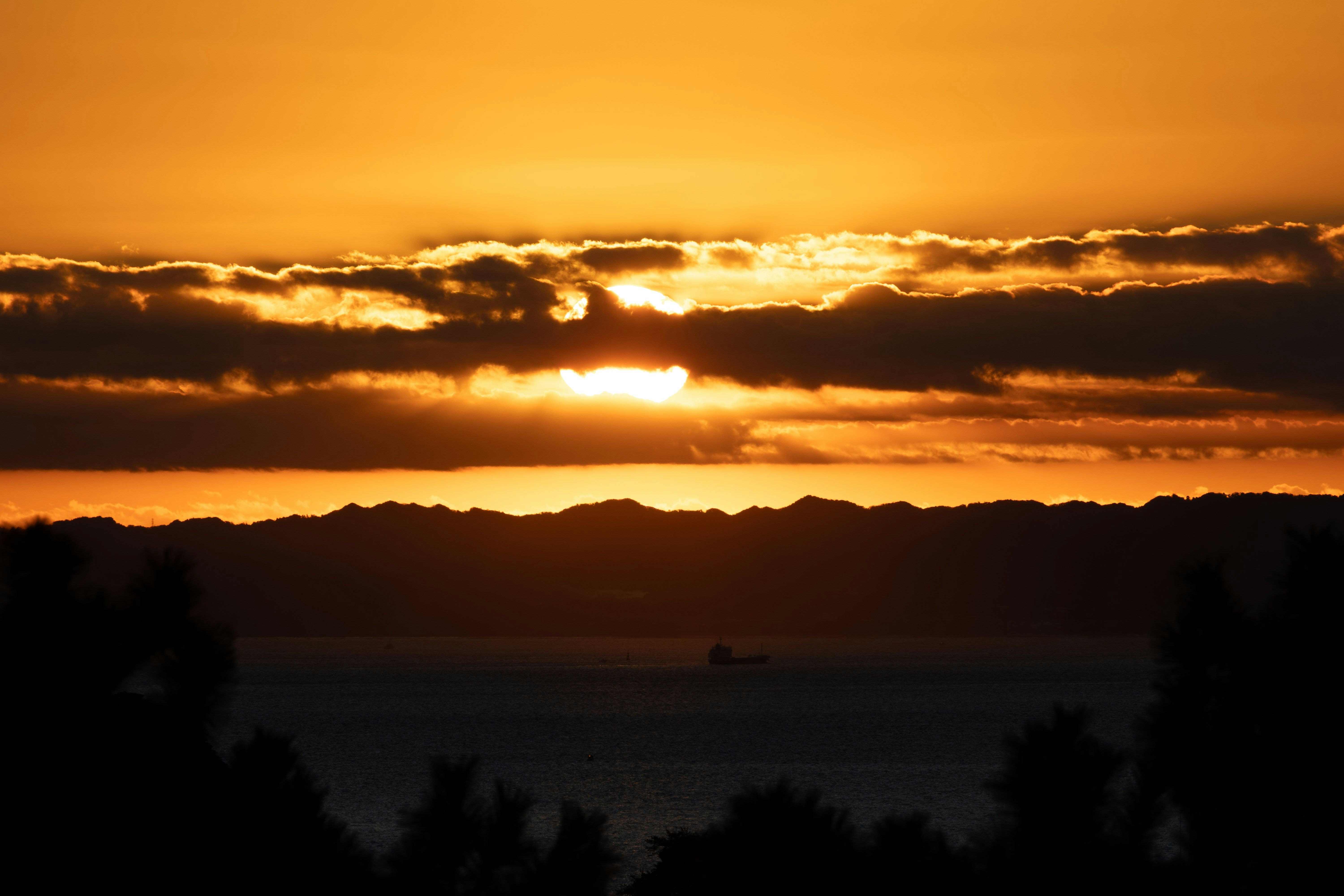 夕焼けの雲と水平線のシルエットが広がる海辺の景色