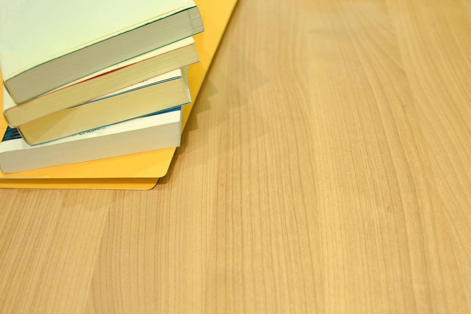 Pila di libri bianchi e una cartella gialla su un tavolo di legno