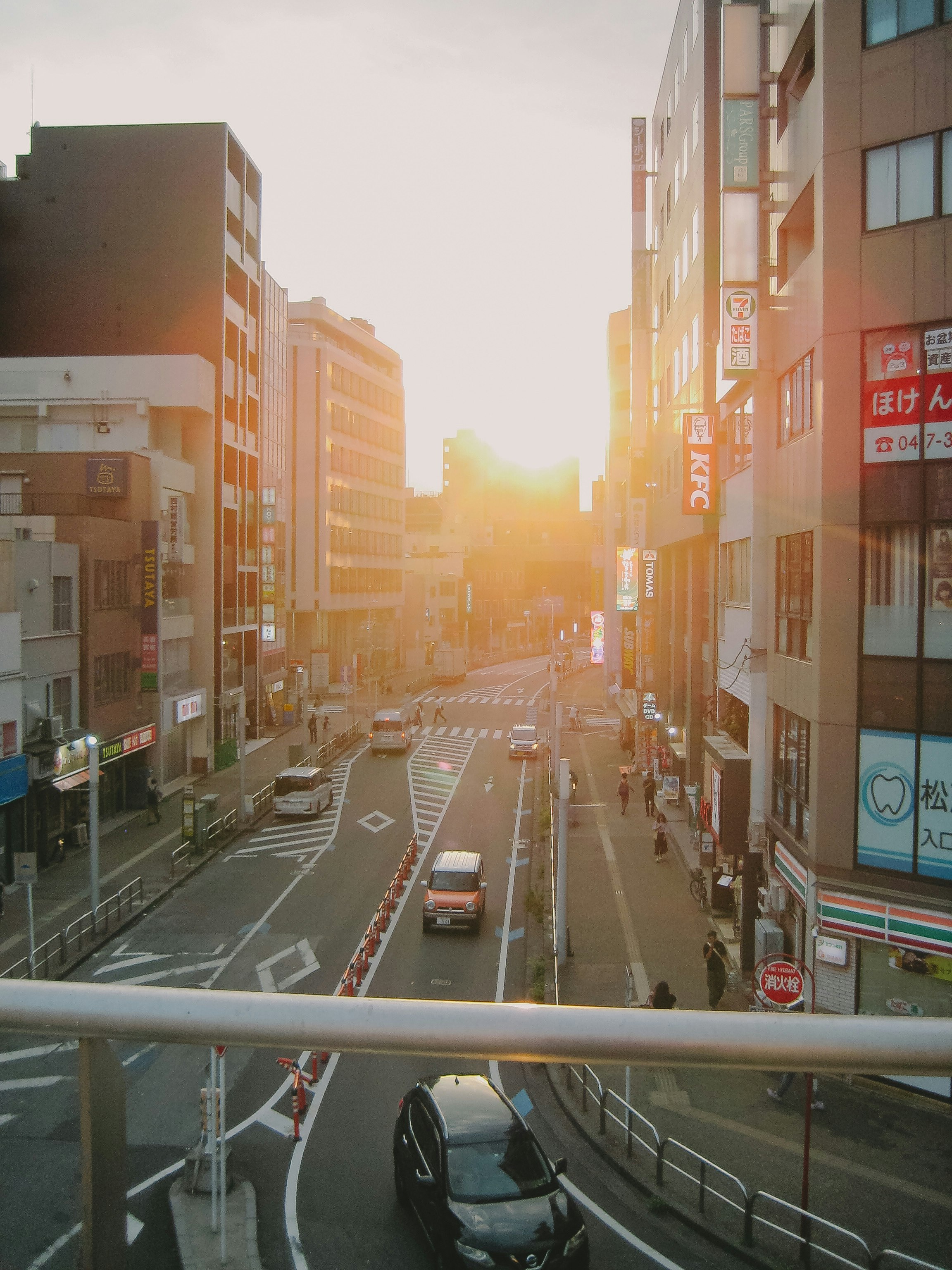 夕日に照らされた商店街の狭い通りと車