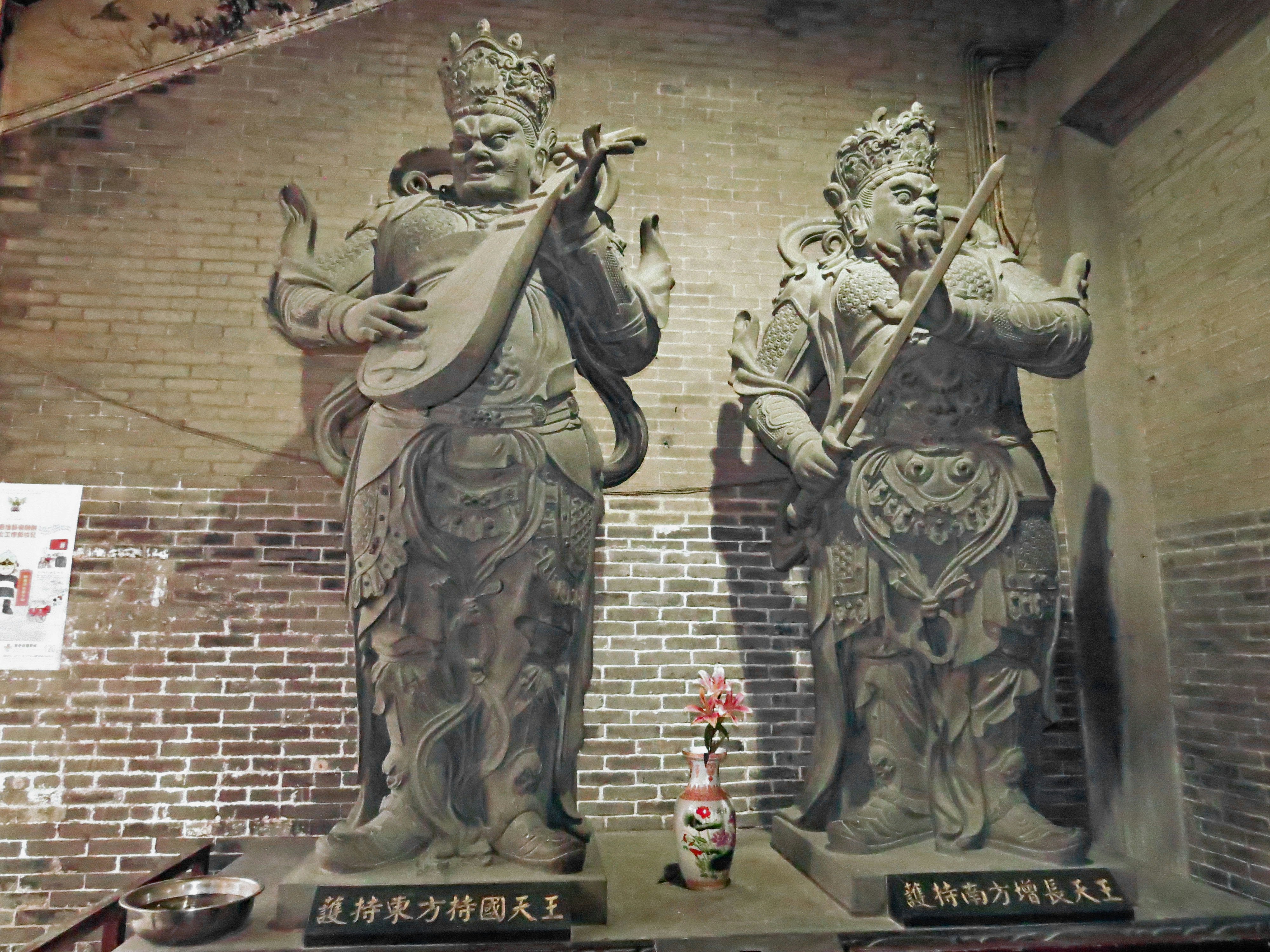 statue di guardiani in metallo davanti a un muro di mattoni in un tempio