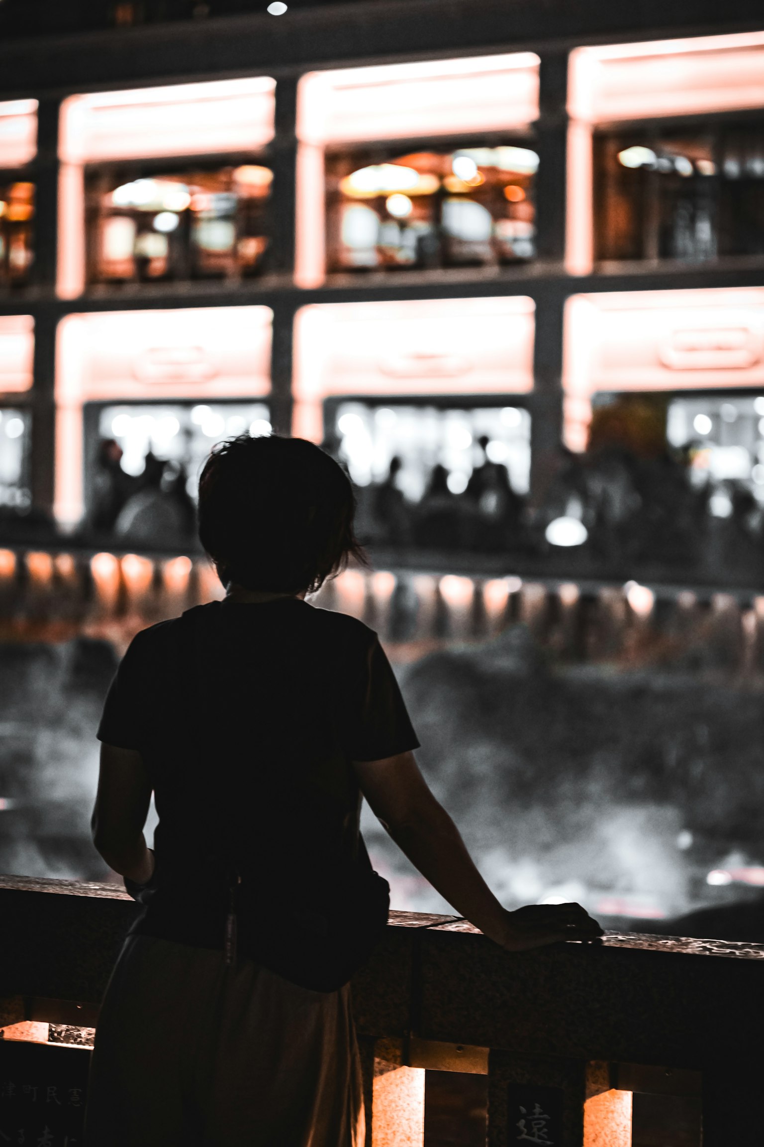 Silhouette of a person gazing at a cityscape at night with illuminated windows