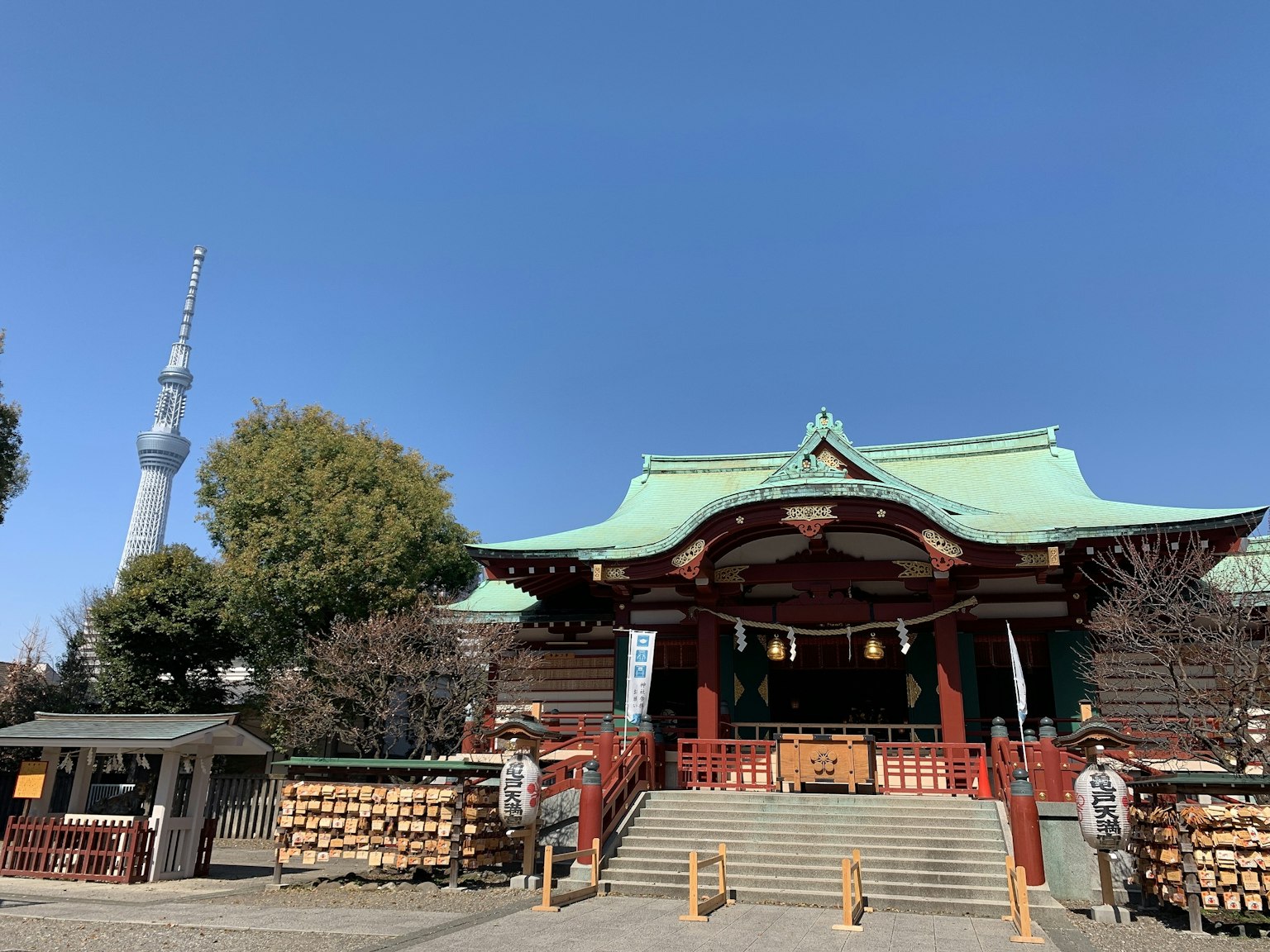 Bâtiment de sanctuaire traditionnel avec un toit vert et Tokyo Skytree en arrière-plan sous un ciel bleu clair