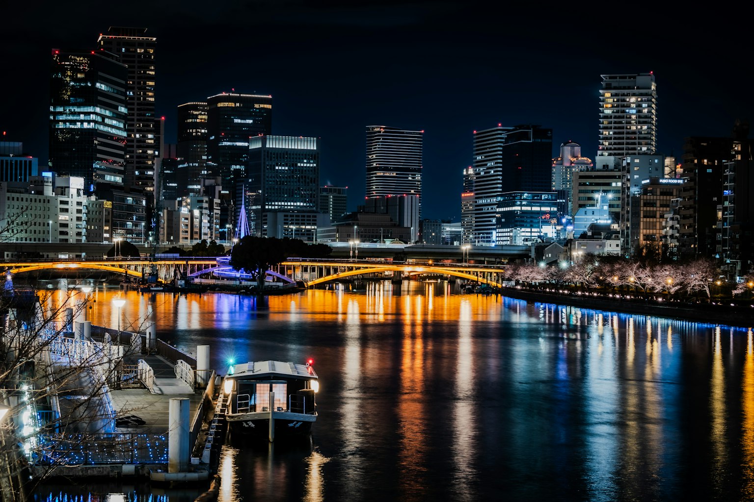 Nighttime cityscape with illuminated skyscrapers and bridge reflecting on water