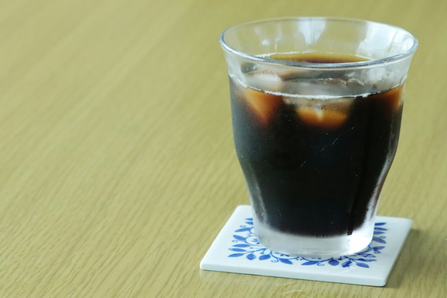 Sebuah gelas transparan berisi kopi es di atas meja kayu