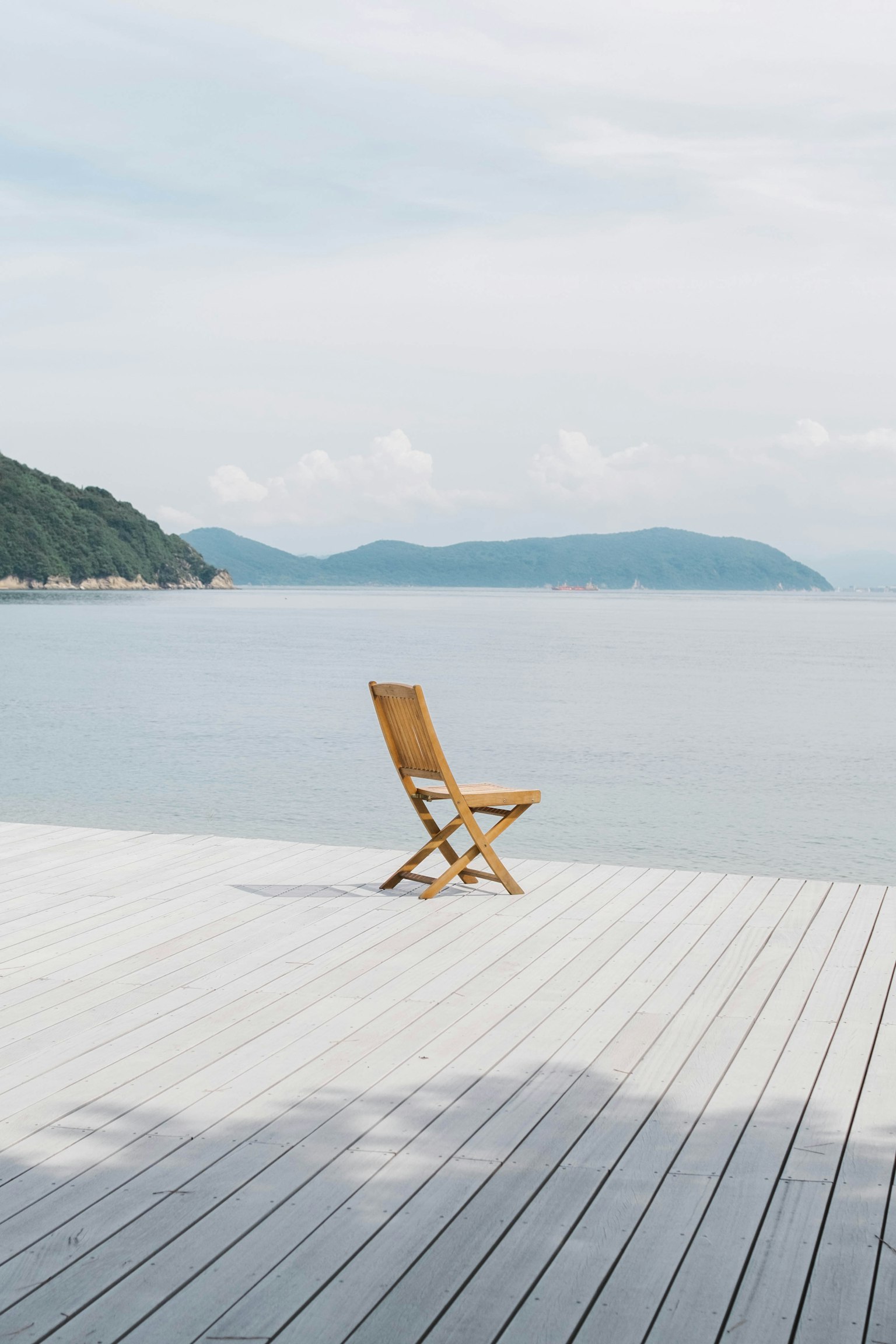 A wooden folding chair on a deck near a calm sea
