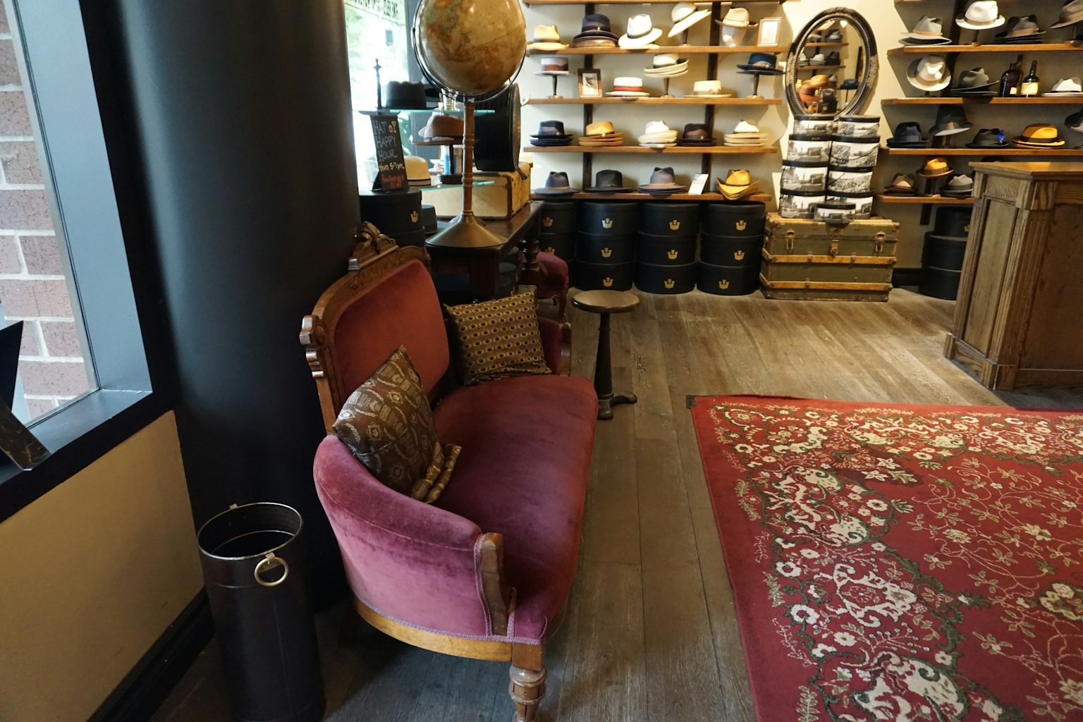 Vintage rosa Sofa mit dekorativen Kissen auf einem roten Teppich neben Regalen voller Hüte