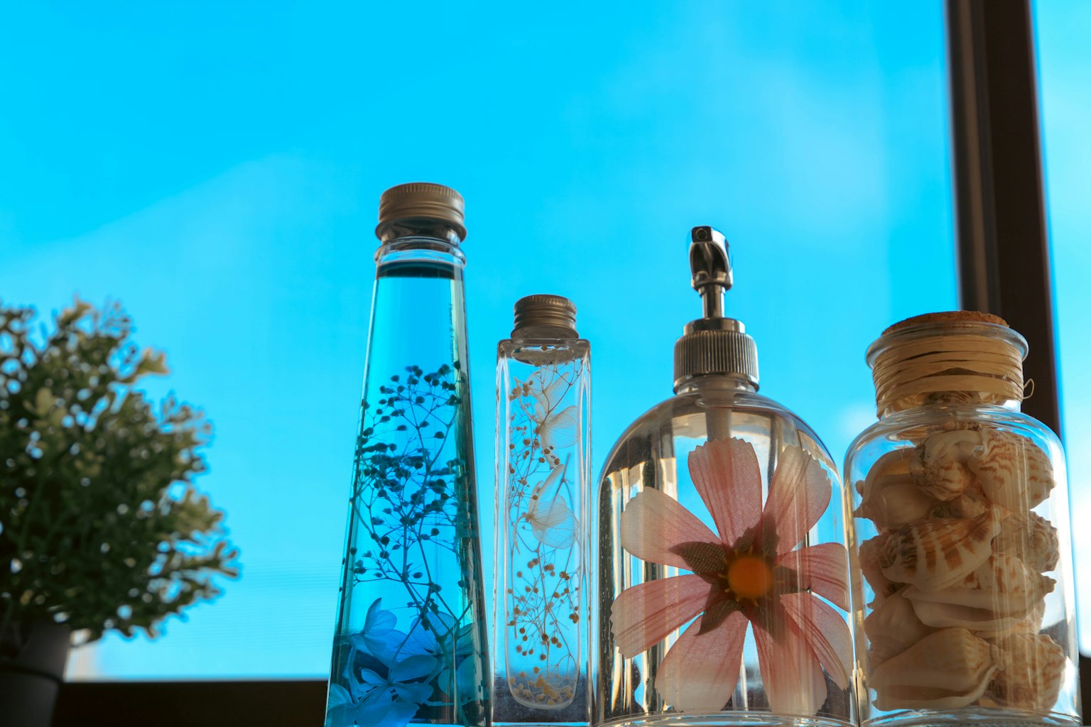 Klare Flaschen mit blauer Flüssigkeit und Blumendekoration vor blauem Himmel